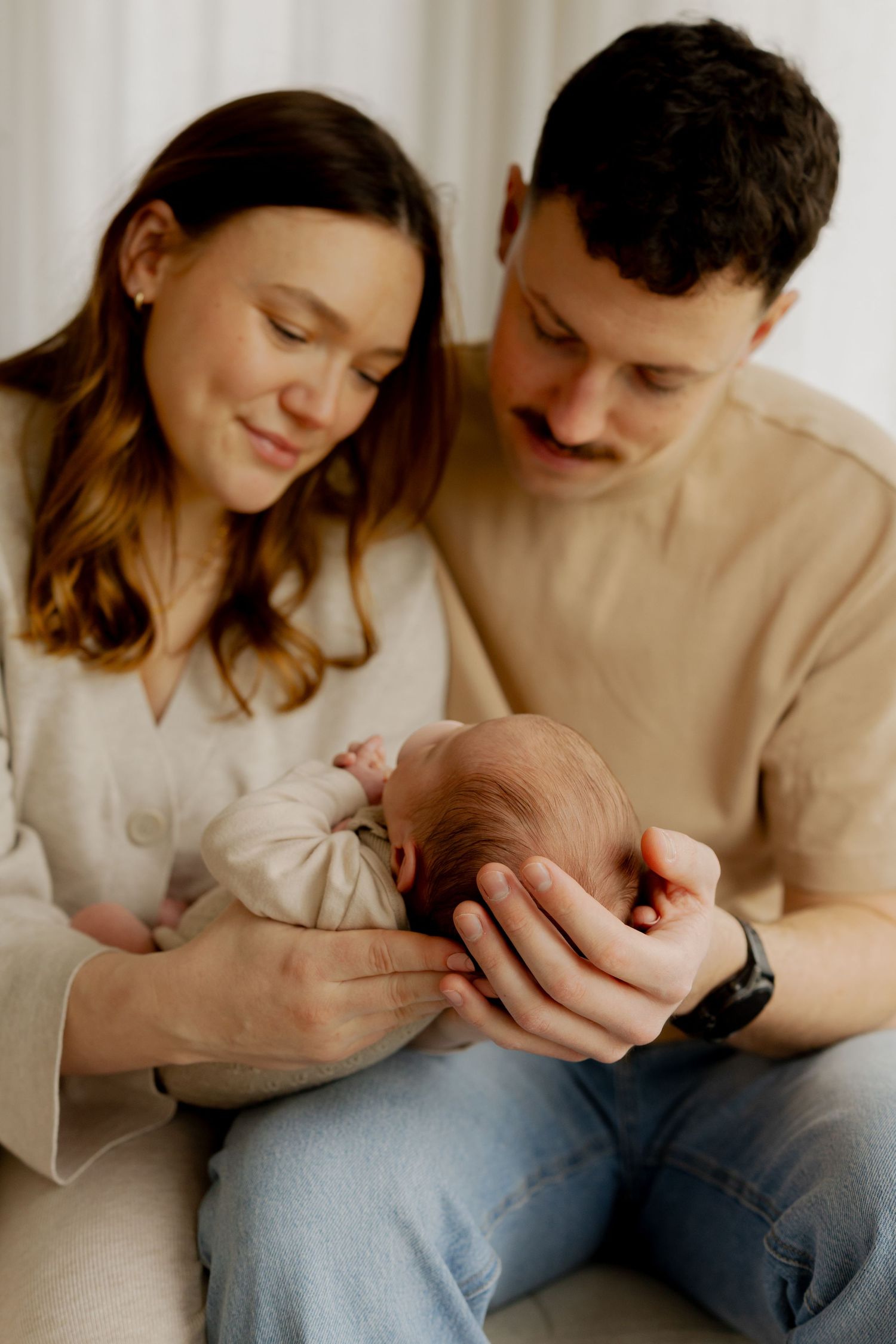 Couple in neutral tones sitting close together on couch sharing intimate moments in three connected photos.