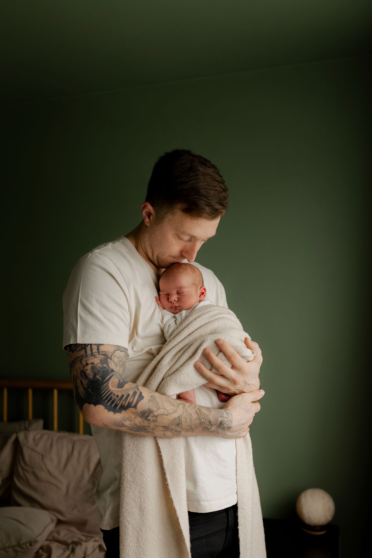 A tender moment captured in soft lighting shows a parent cradling a sleeping newborn baby against white fabric.
