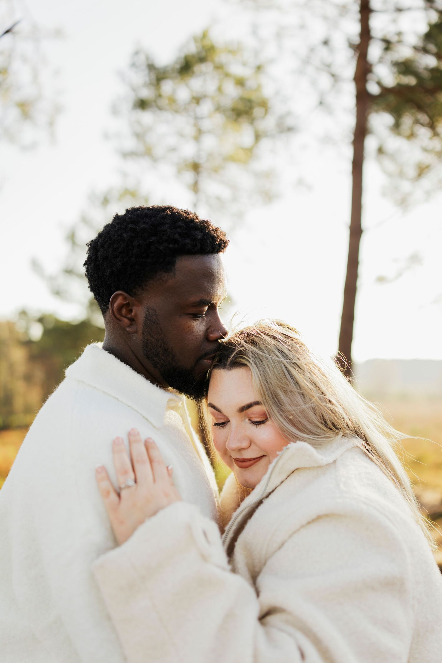Intimate moment between couple wearing matching white sweaters in warm sunset light.