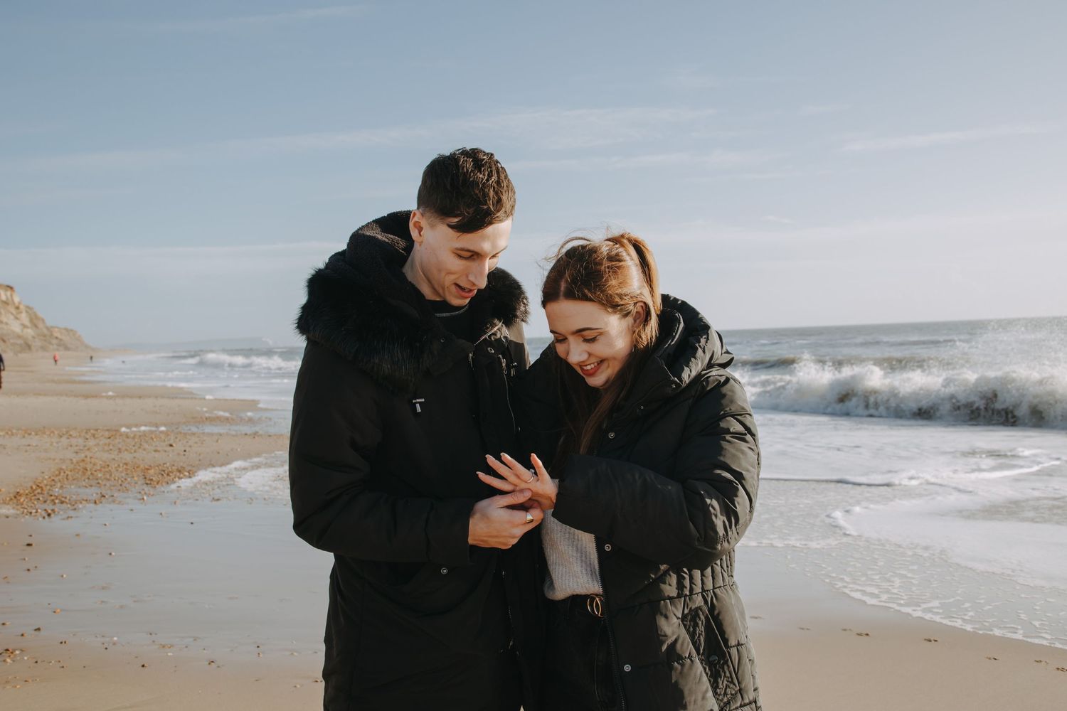 A couple shares an intimate moment while looking at something together on a windy beach.