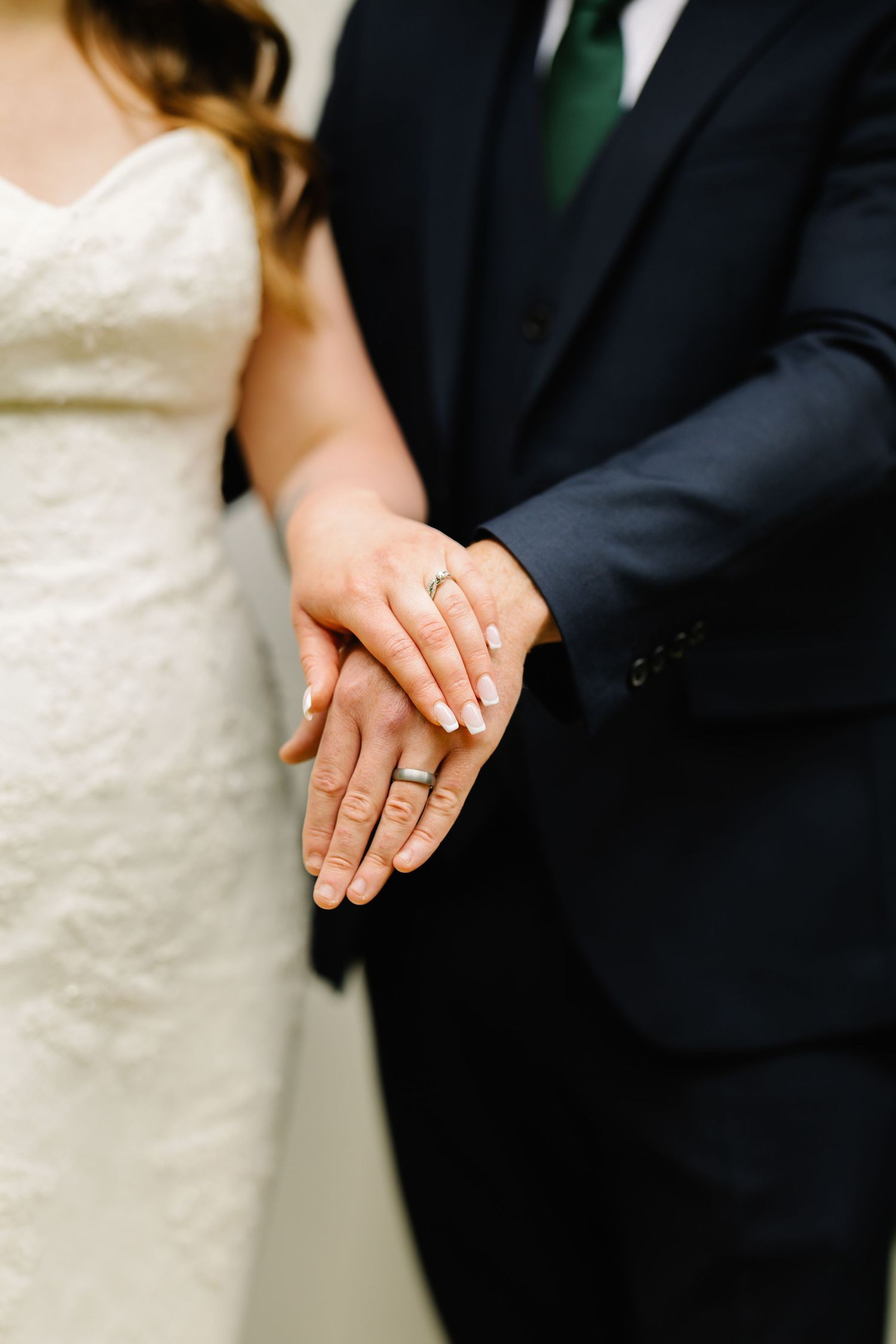 Close-up shot of hands displaying wedding rings against formal attire.