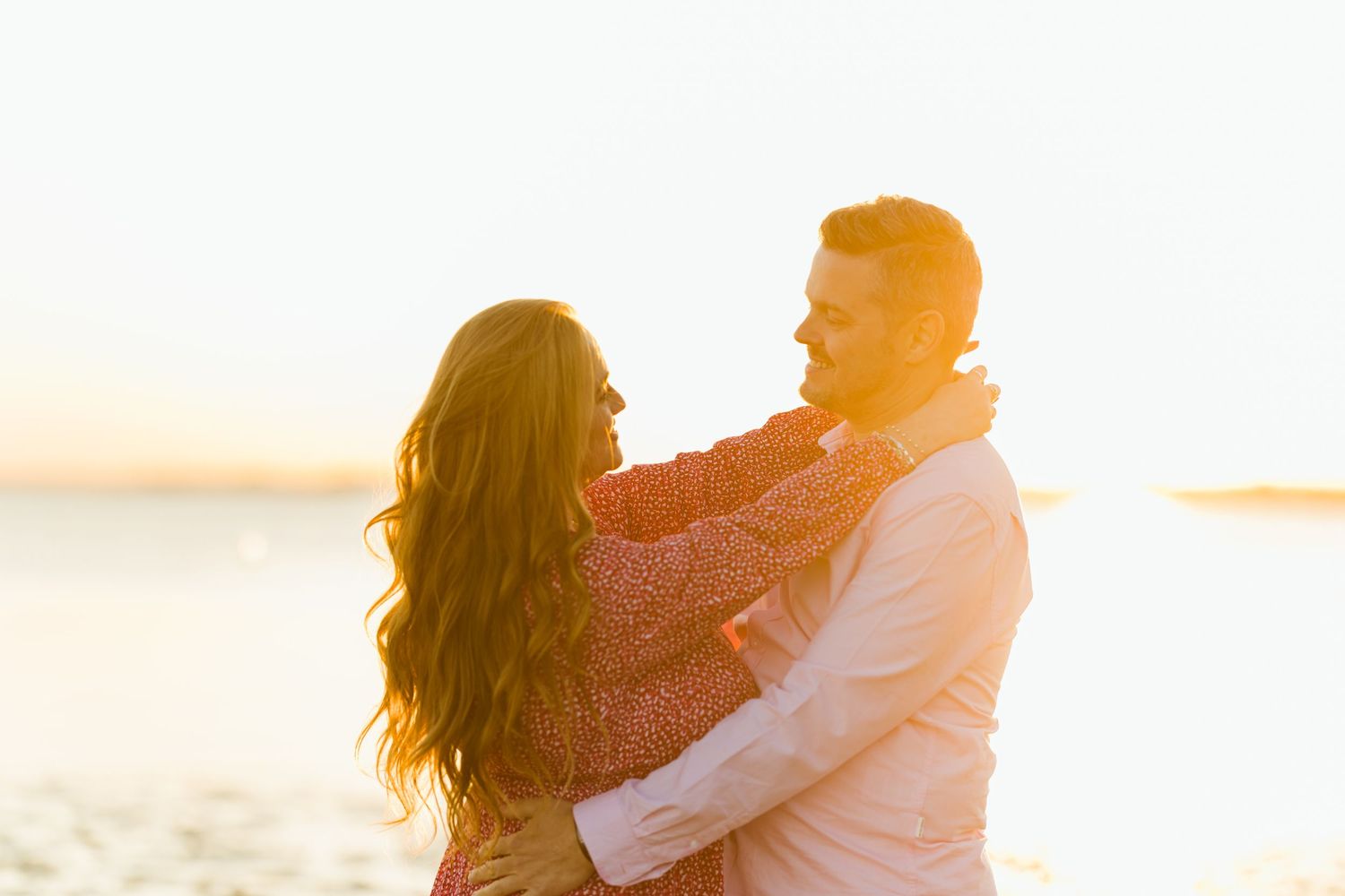 Couple sharing intimate moment on beach during golden hour with backlit silhouette.