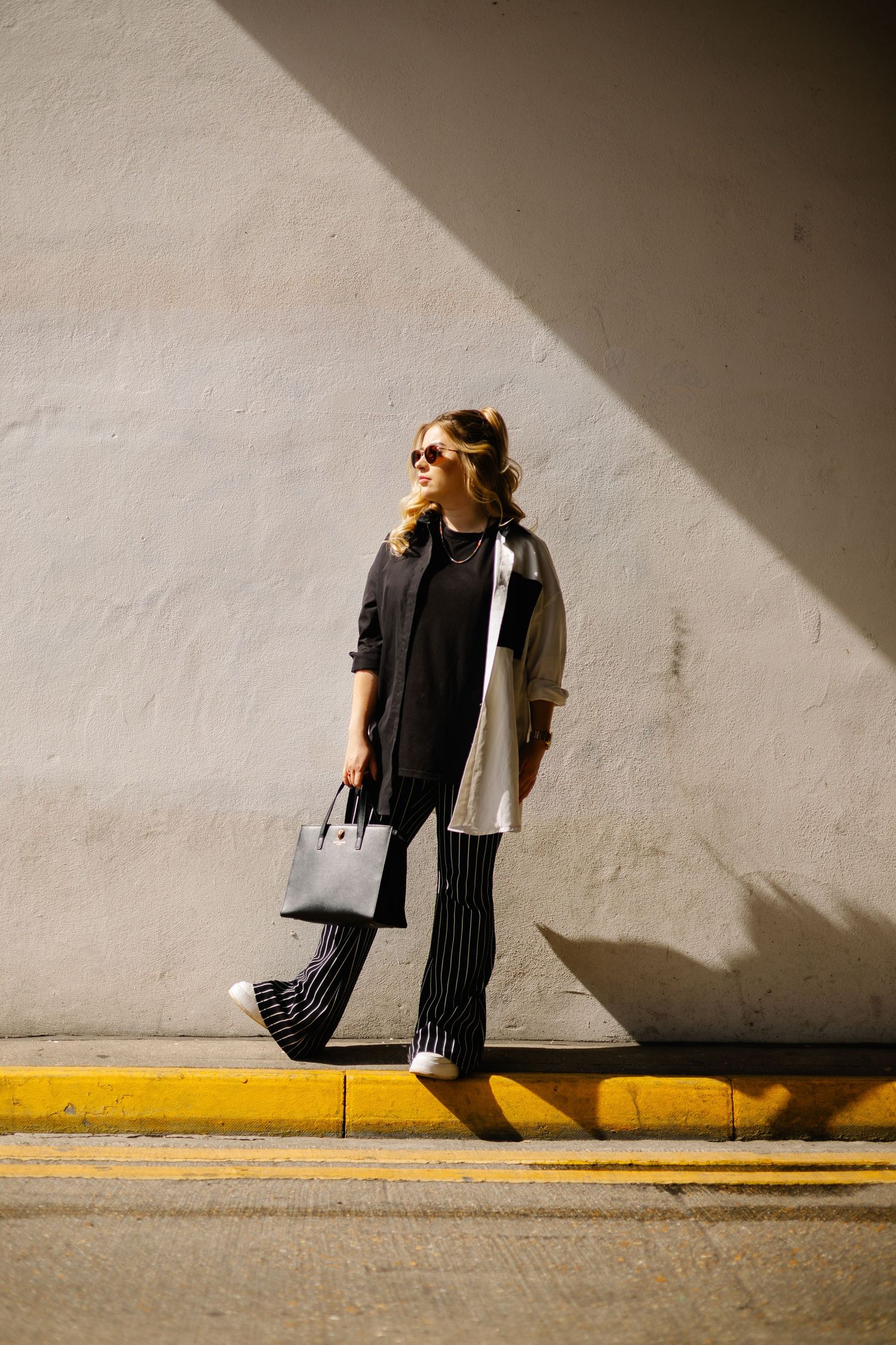 Woman in monochrome outfit poses against wall with dramatic shadow.