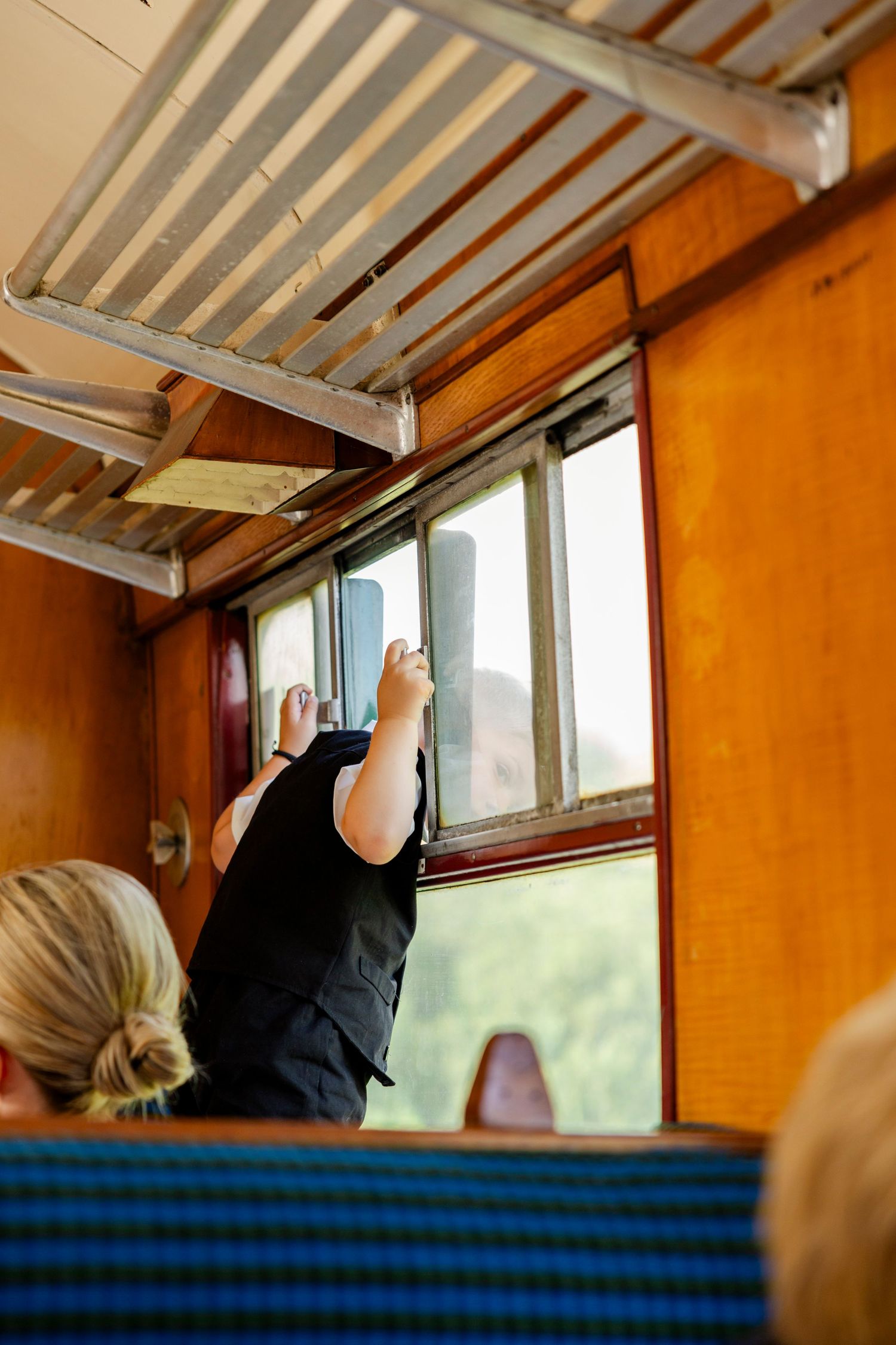 A passenger reaches up to open a window on a vintage train car with orange interior.