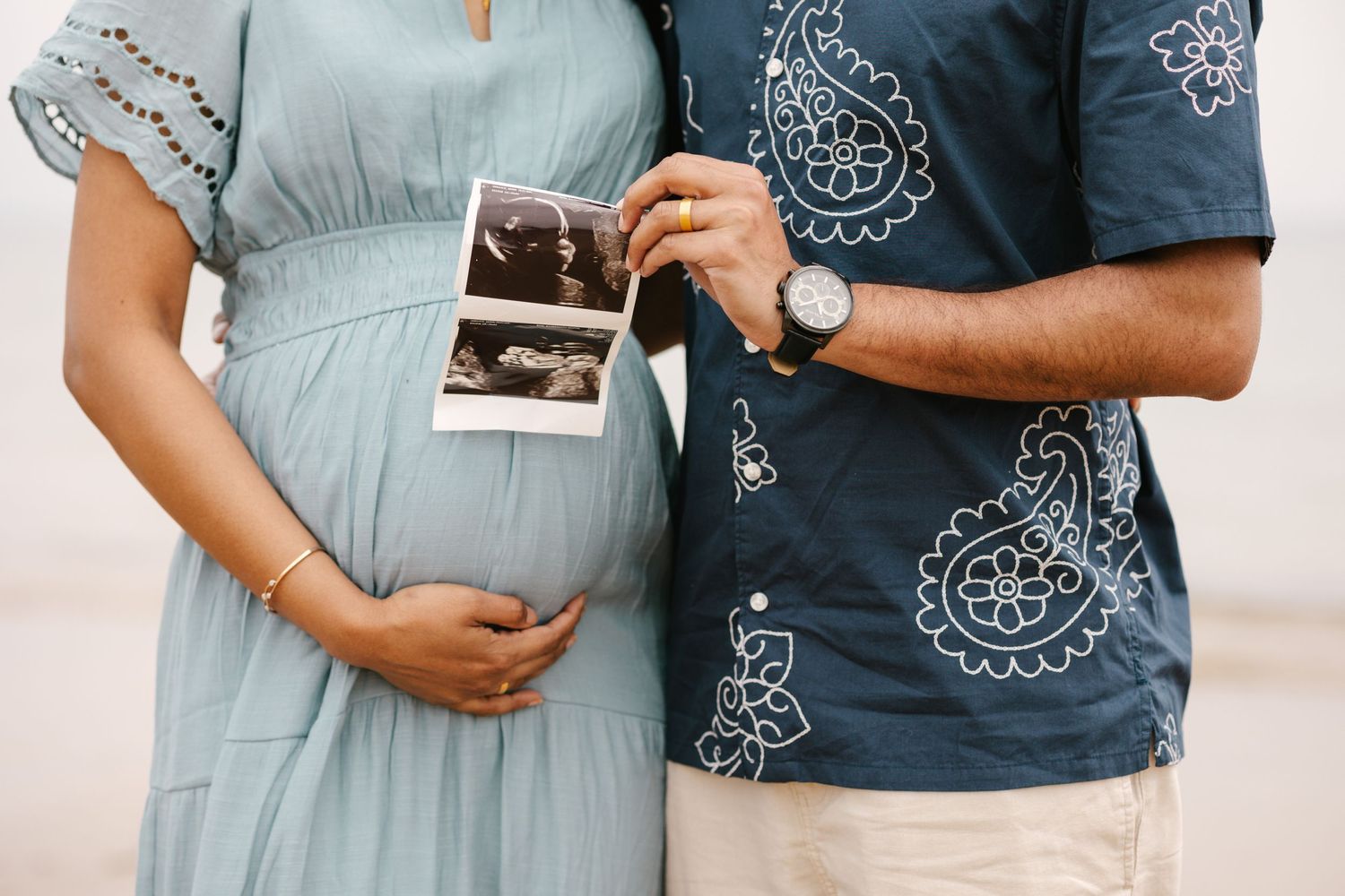 Pregnant couple holding ultrasound photo while standing together outdoors.