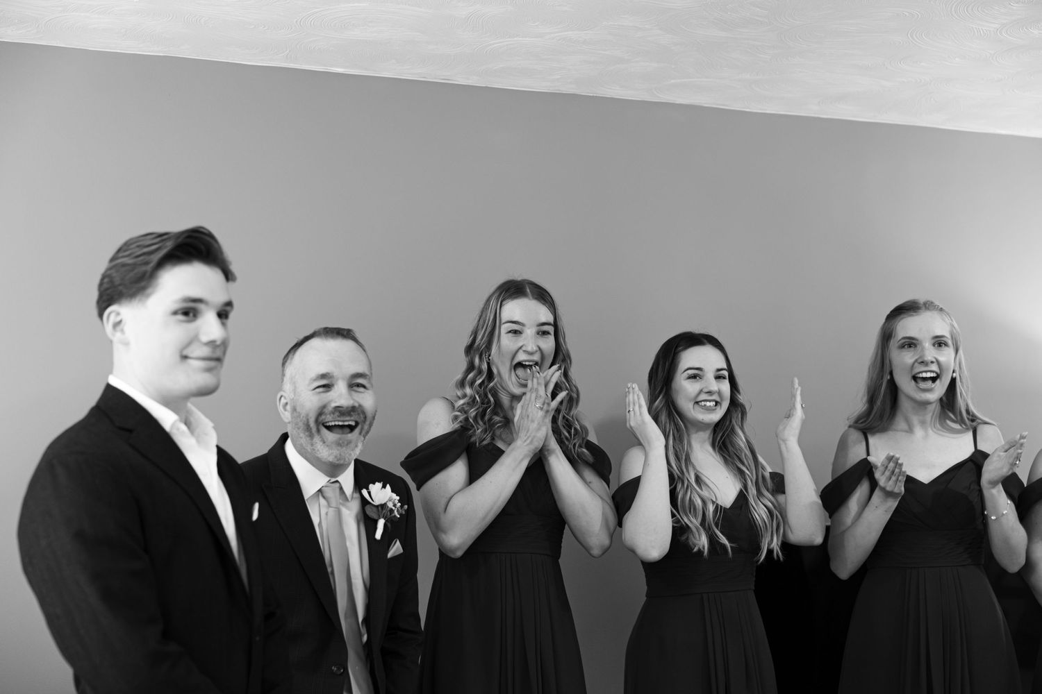 A wedding party reacts with excitement in a black and white group photo.