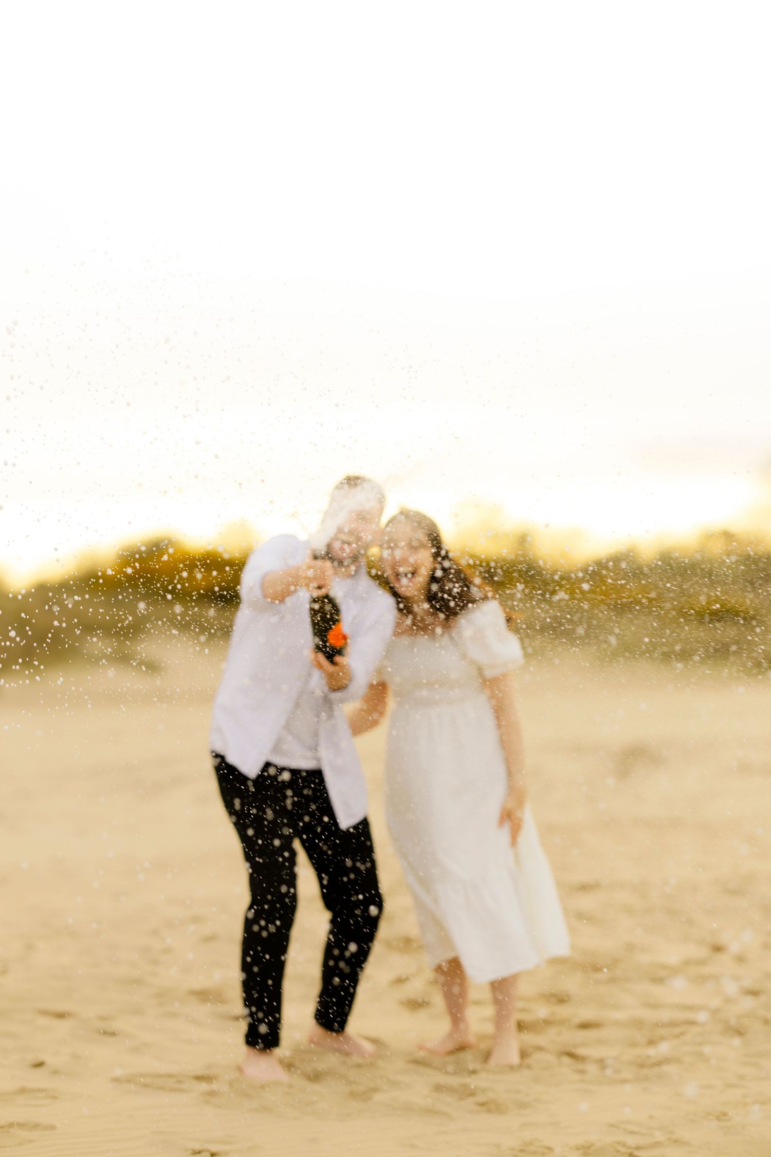 Joyful couple playing in glittering sand during sunset at the beach.