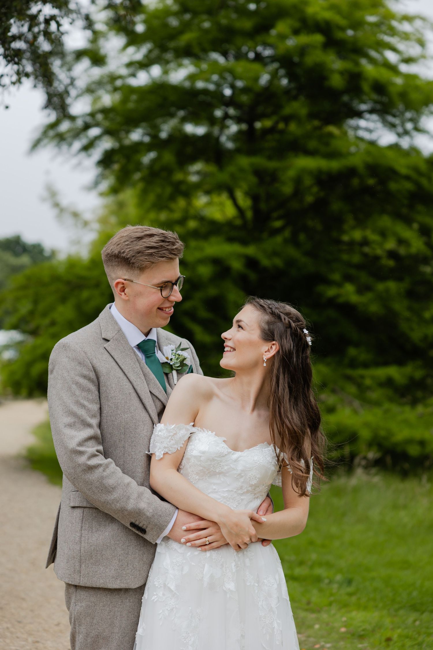 Newlyweds in grey suit and white dress embrace on a garden path.