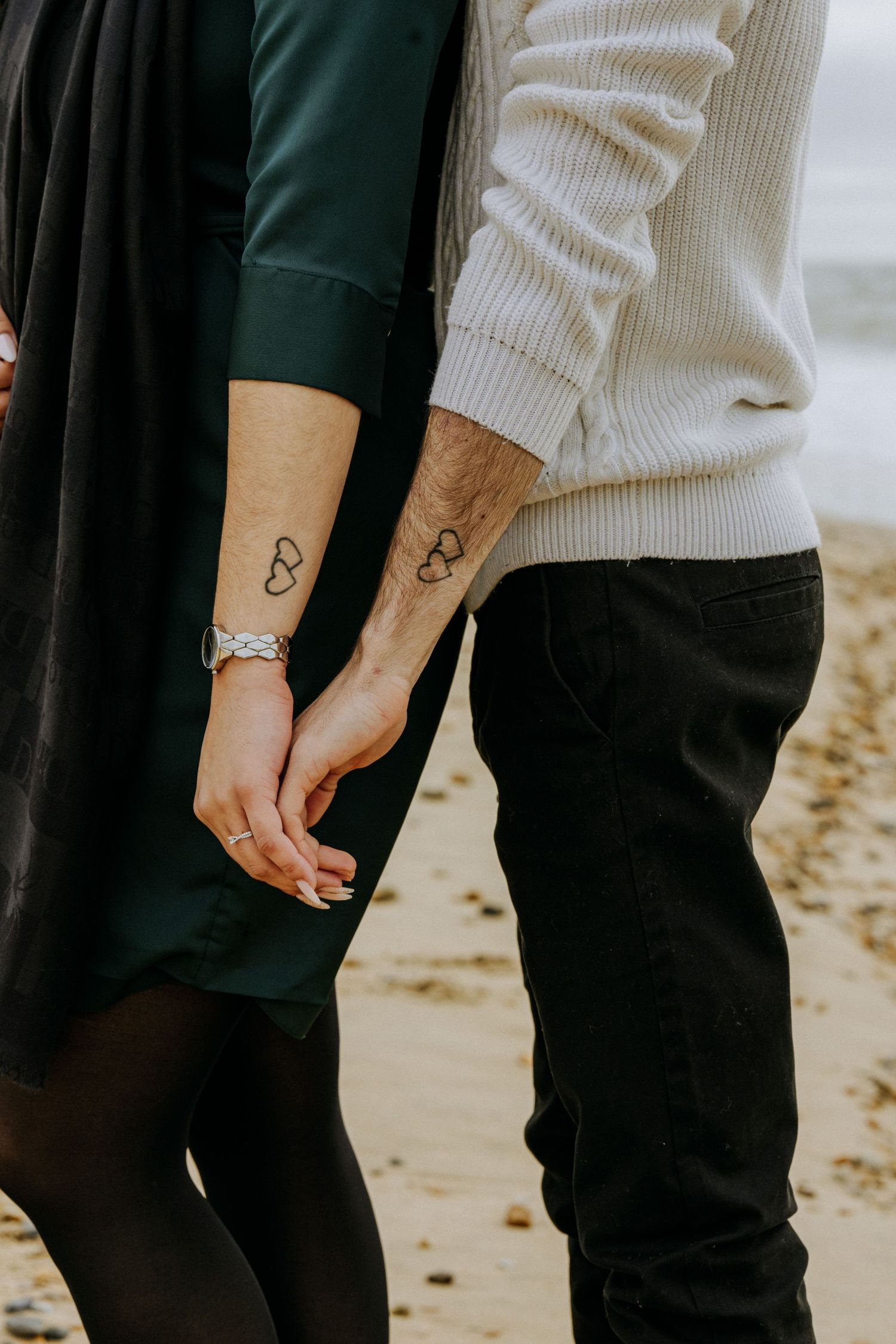 Close-up of matching infinity tattoos on two arms against casual clothing.