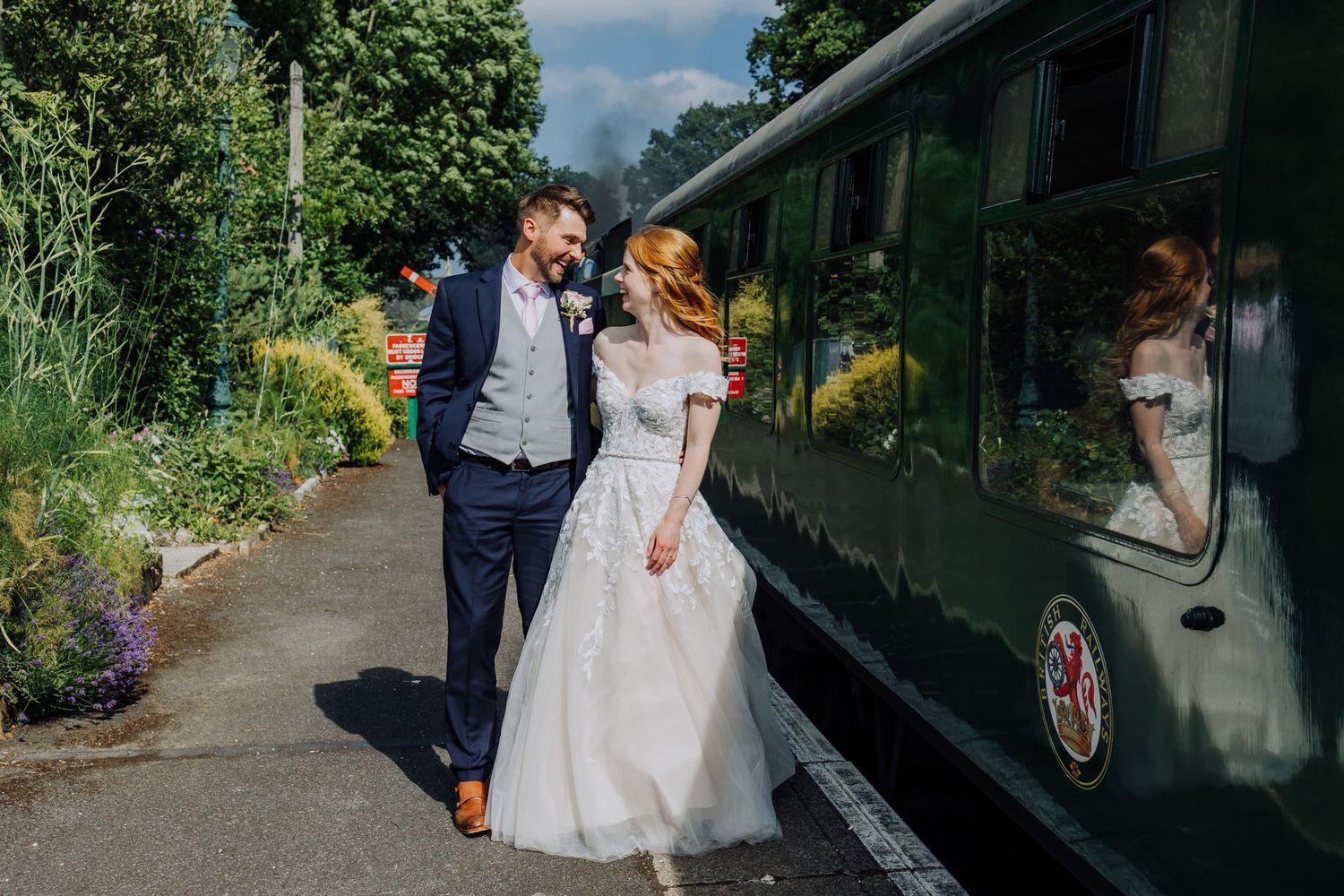 Newlyweds walking together alongside a vintage train car on their wedding day.