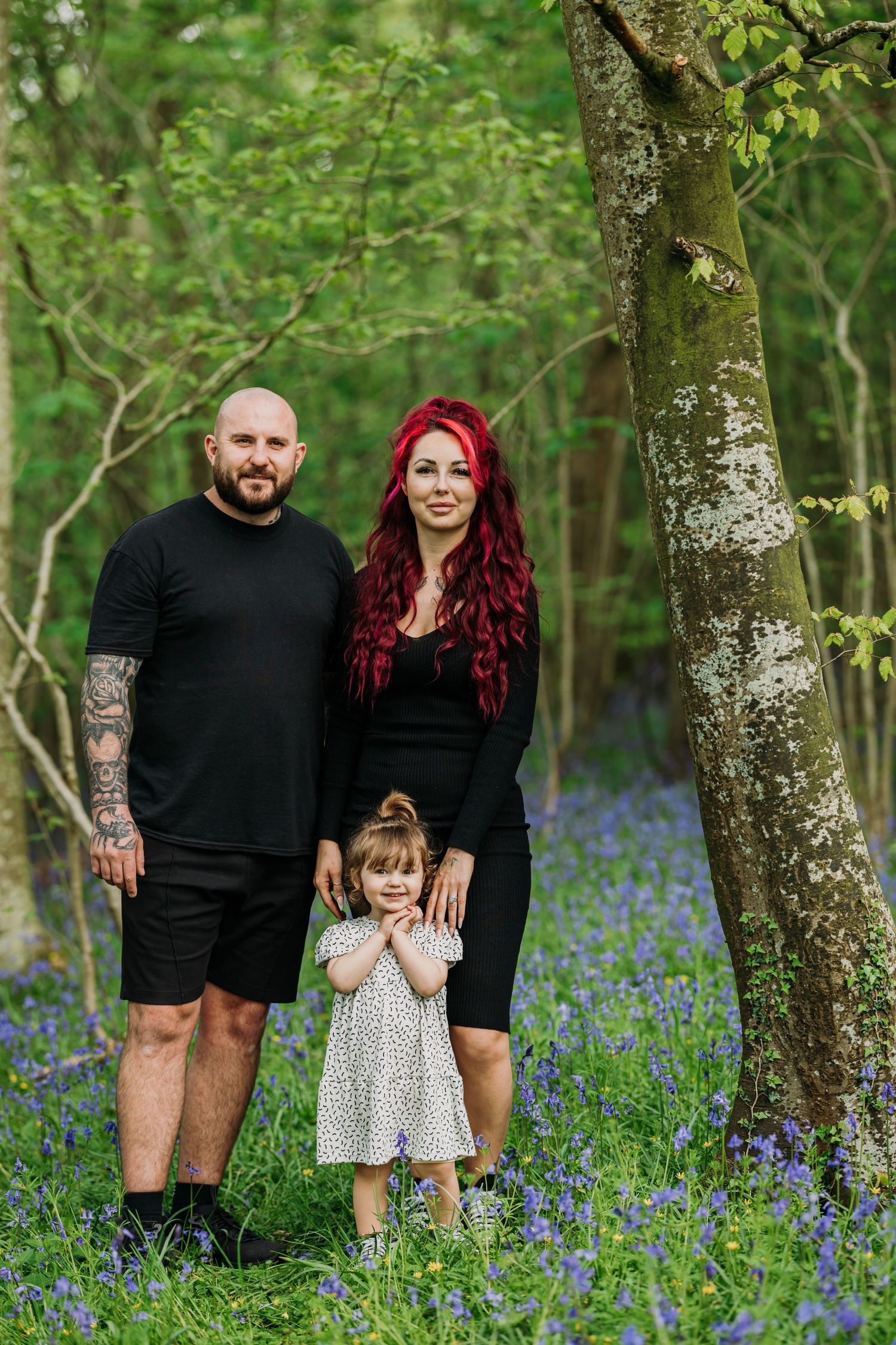 Family standing among blooming bluebells in lush woodland setting.