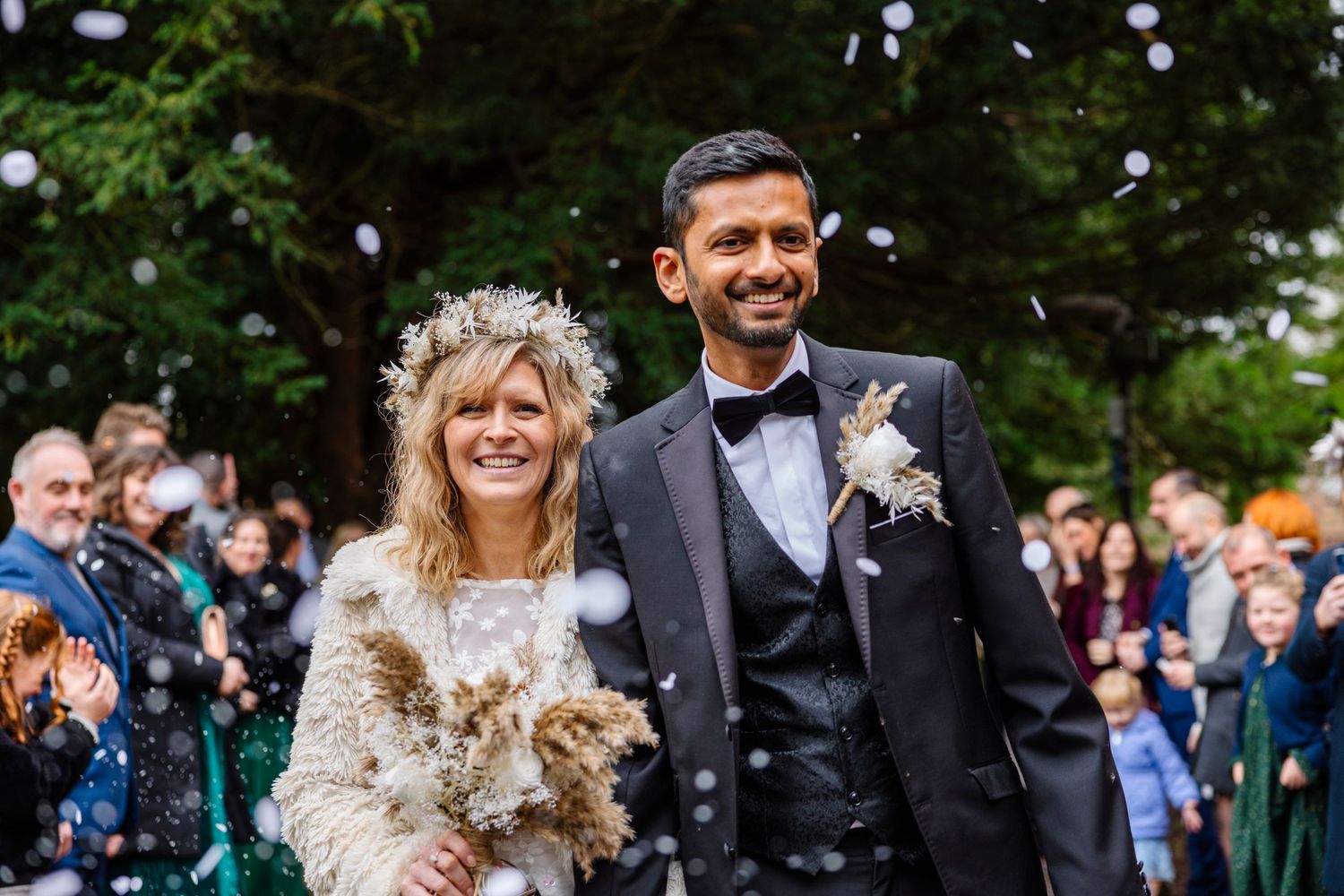 Happy couple exits church ceremony with guests celebrating behind them.