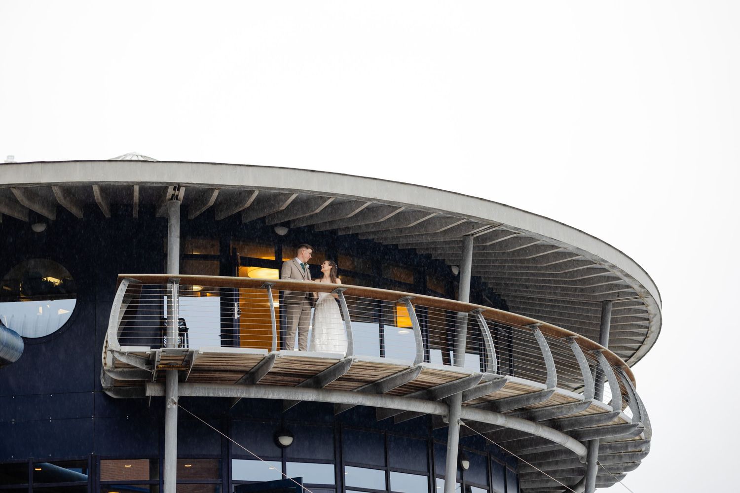Wedding party standing on curved balcony of modern architectural structure.