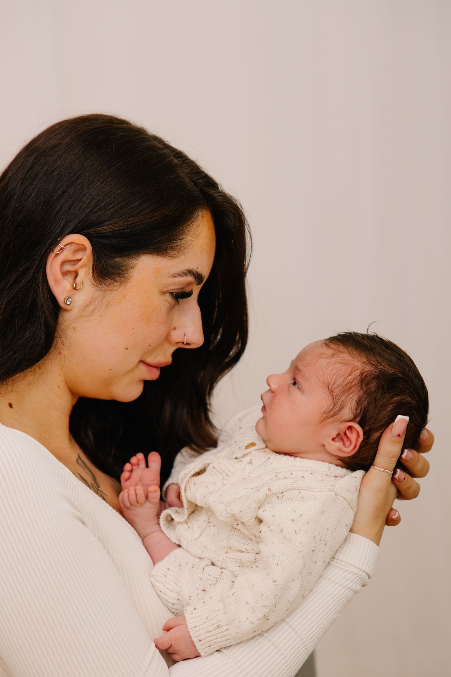 Mother in white sweater holding newborn baby against neutral background in tender portrait.