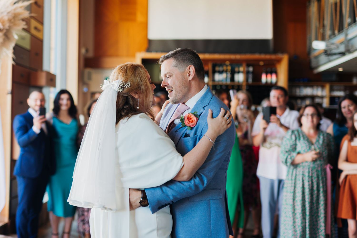 Newlyweds share their first dance surrounded by wedding guests in colorful attire.