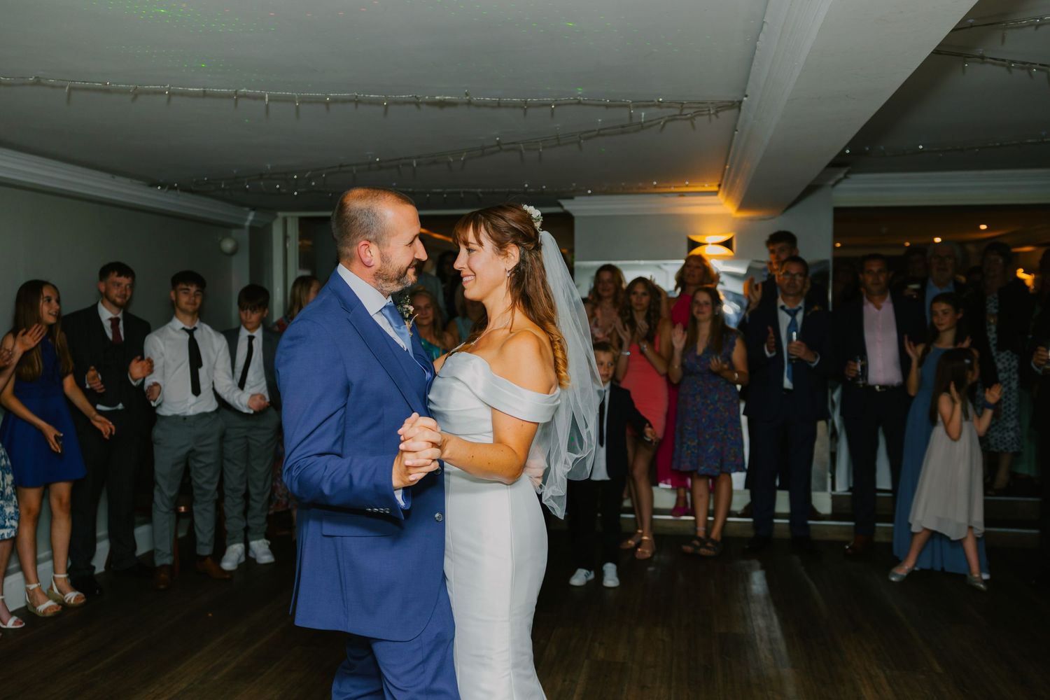 A couple shares their first dance at a wedding reception while guests watch from the background.