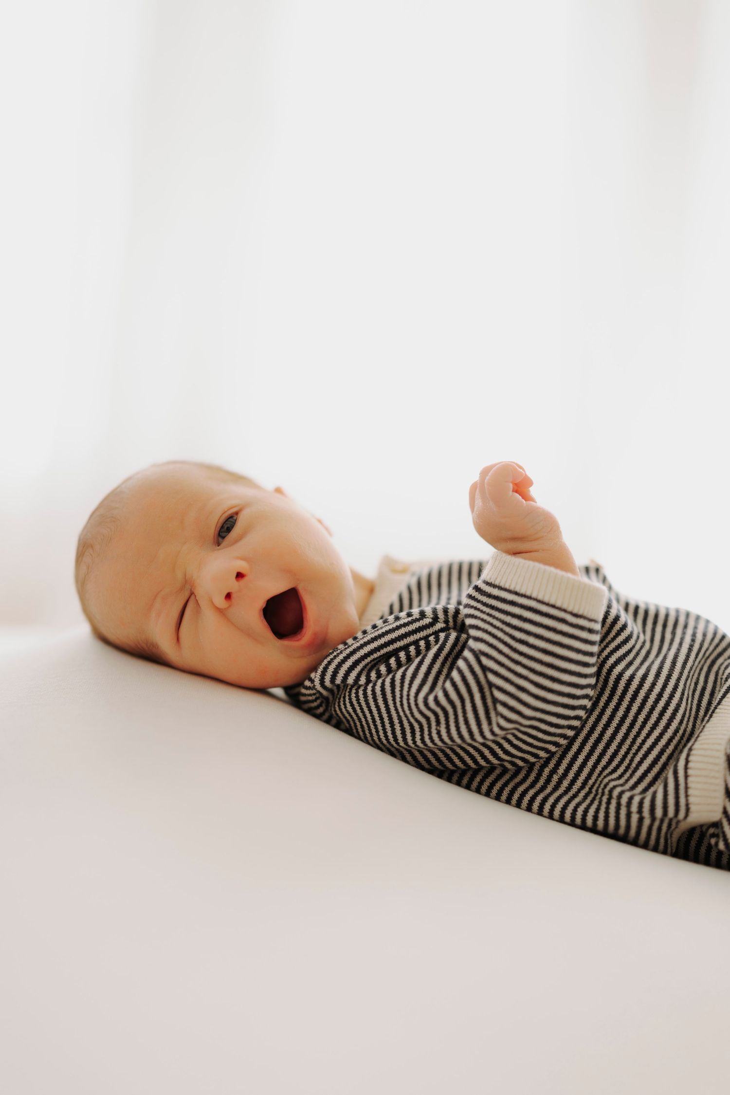 Baby yawning while lying on white surface wearing black and white striped outfit.