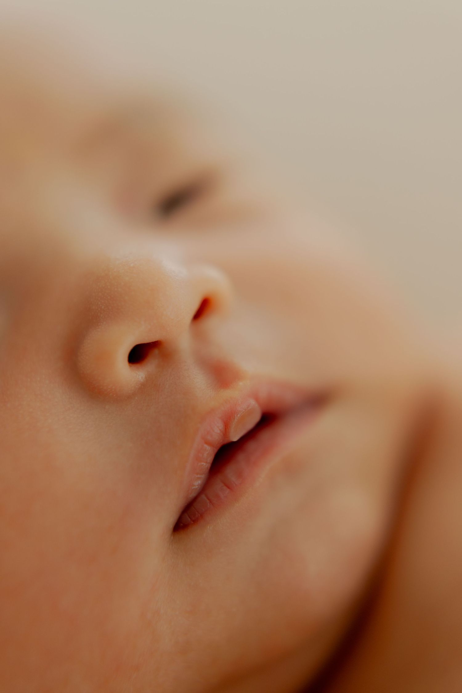 Close-up macro photo of a sleeping newborn baby's nose and lips with soft focus background.