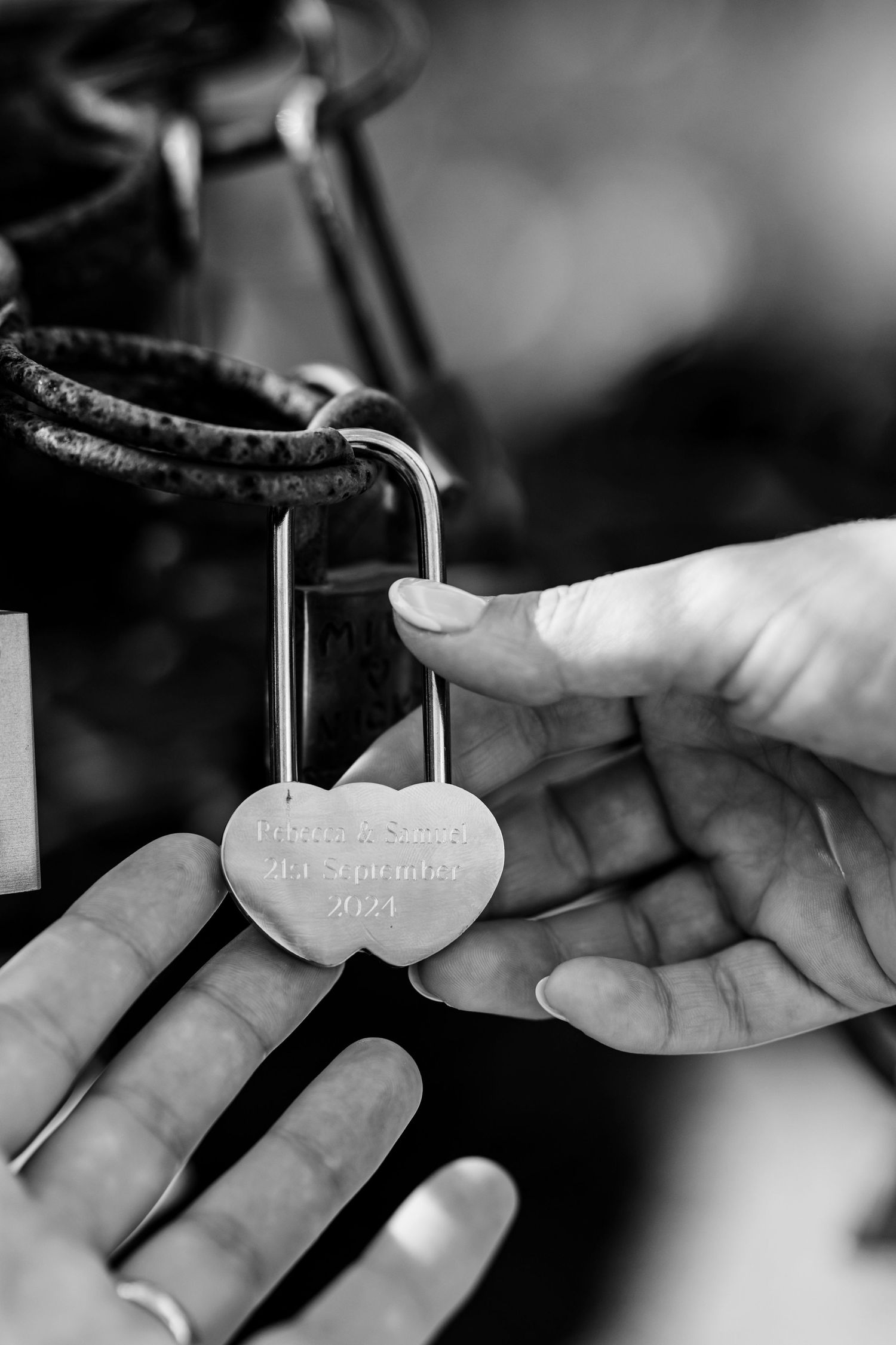 Close-up of hands holding a love lock with engraved text in black and white.