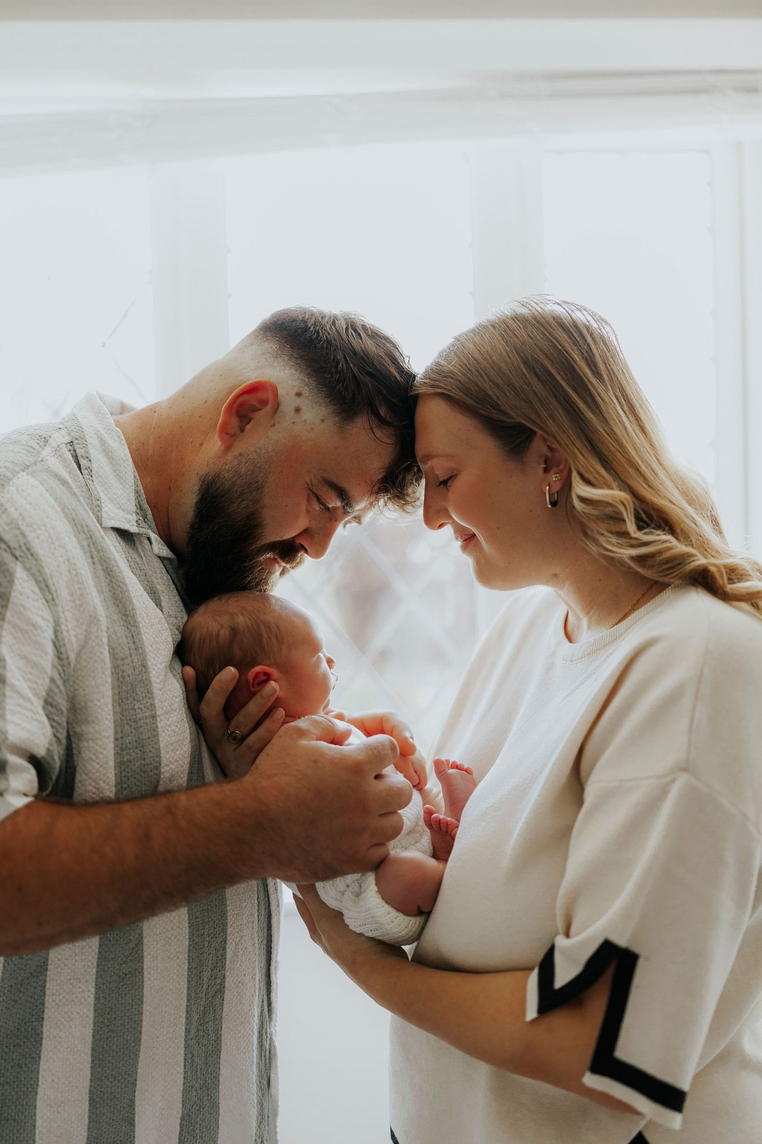 Intimate family moment with parents gazing lovingly at their newborn baby against white background.