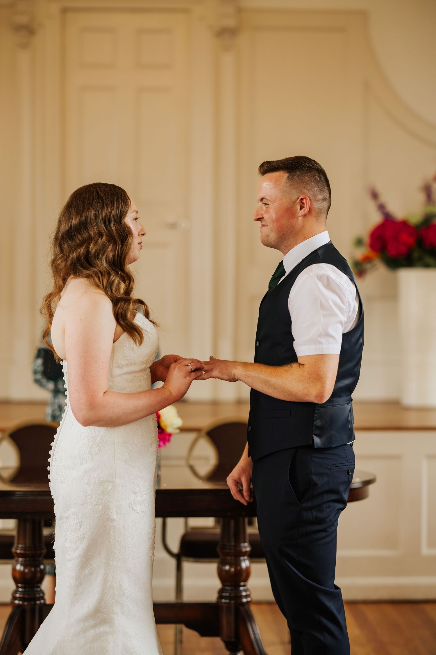 A tender moment between a couple during their first look in an elegant indoor venue with white walls and red floral accents.