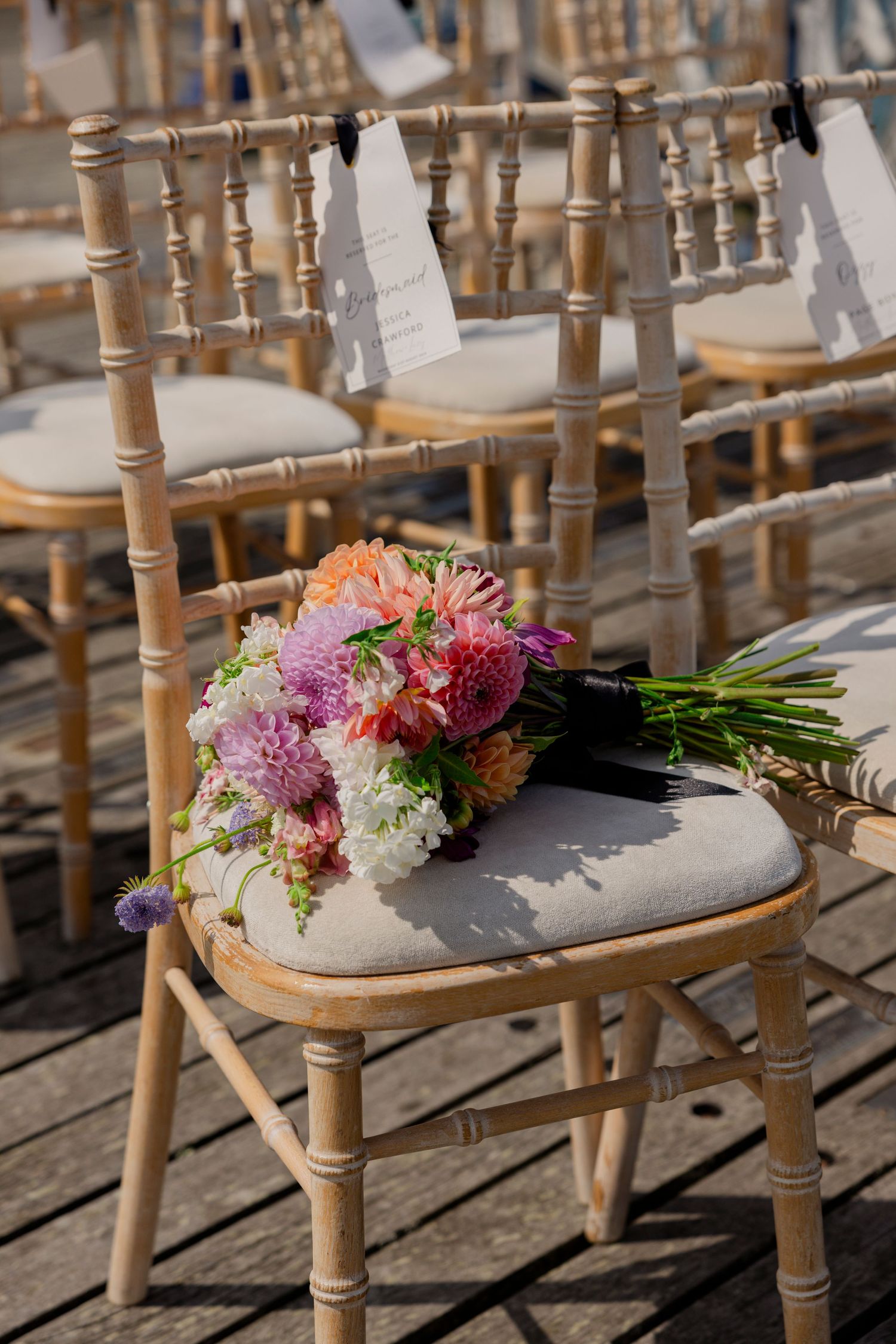 Colorful floral bouquet on wooden Chiavari chair at outdoor wedding venue.
