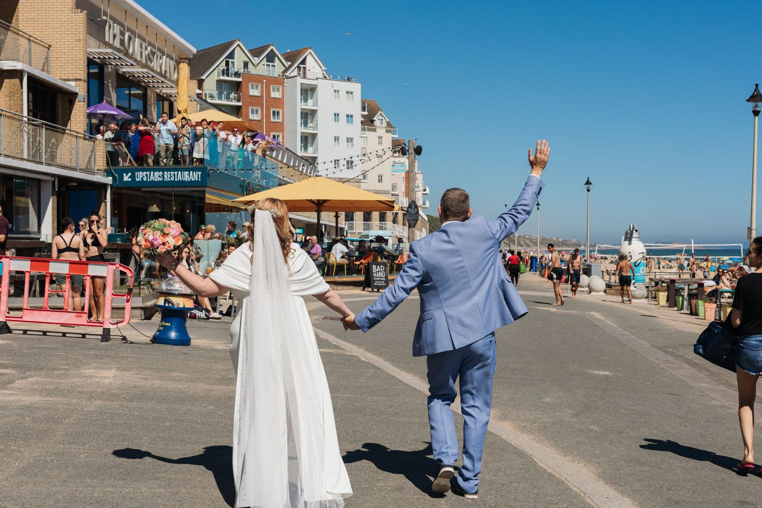 Couple celebrating on a beachfront boardwalk with buildings in the background.