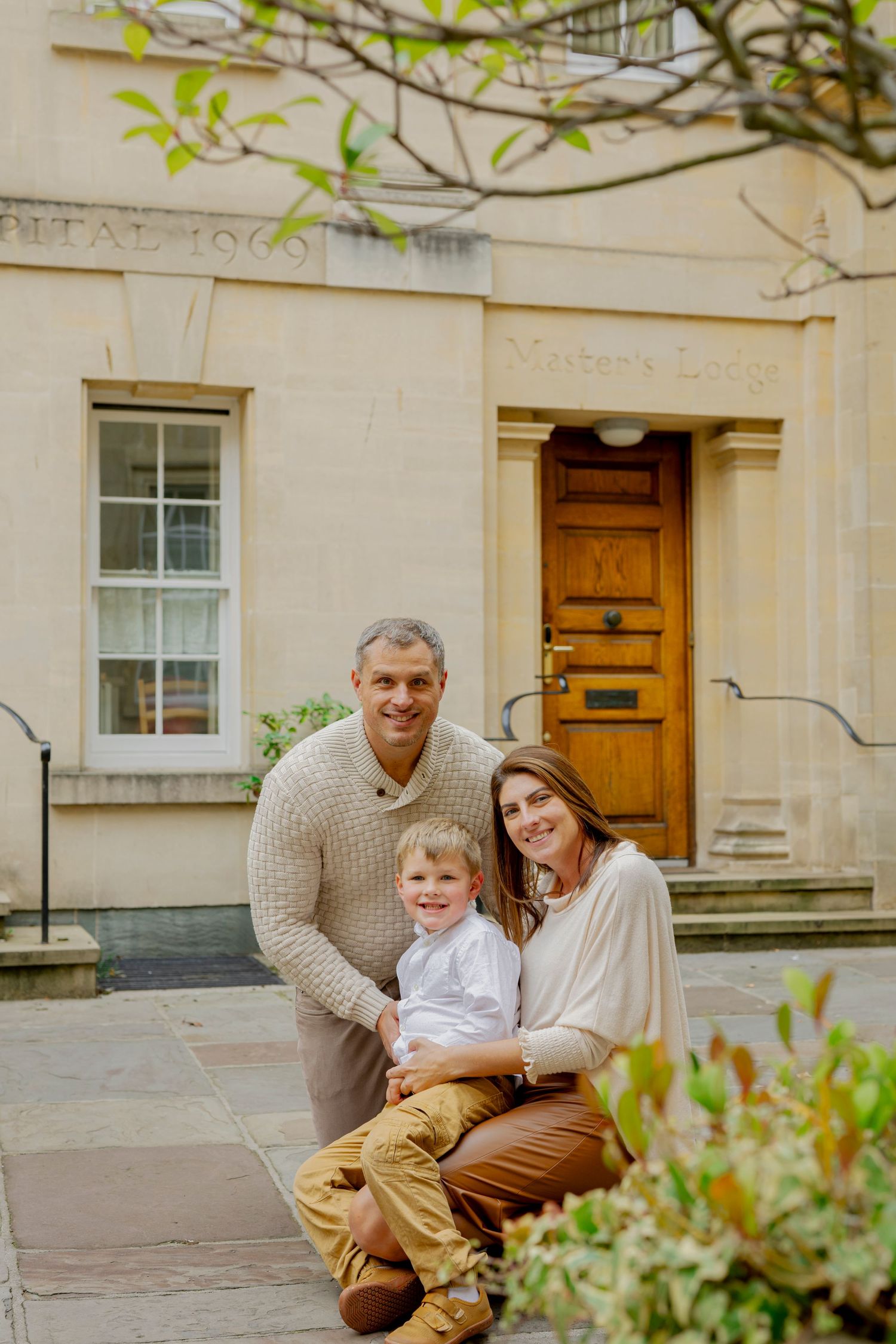 Happy family of three posing outside a historic stone building with Master's Lodge entrance door.