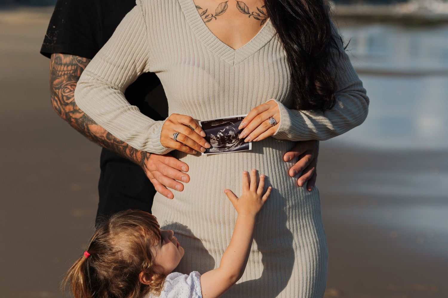 Family looking at ultrasound photos together on beach during sunset.