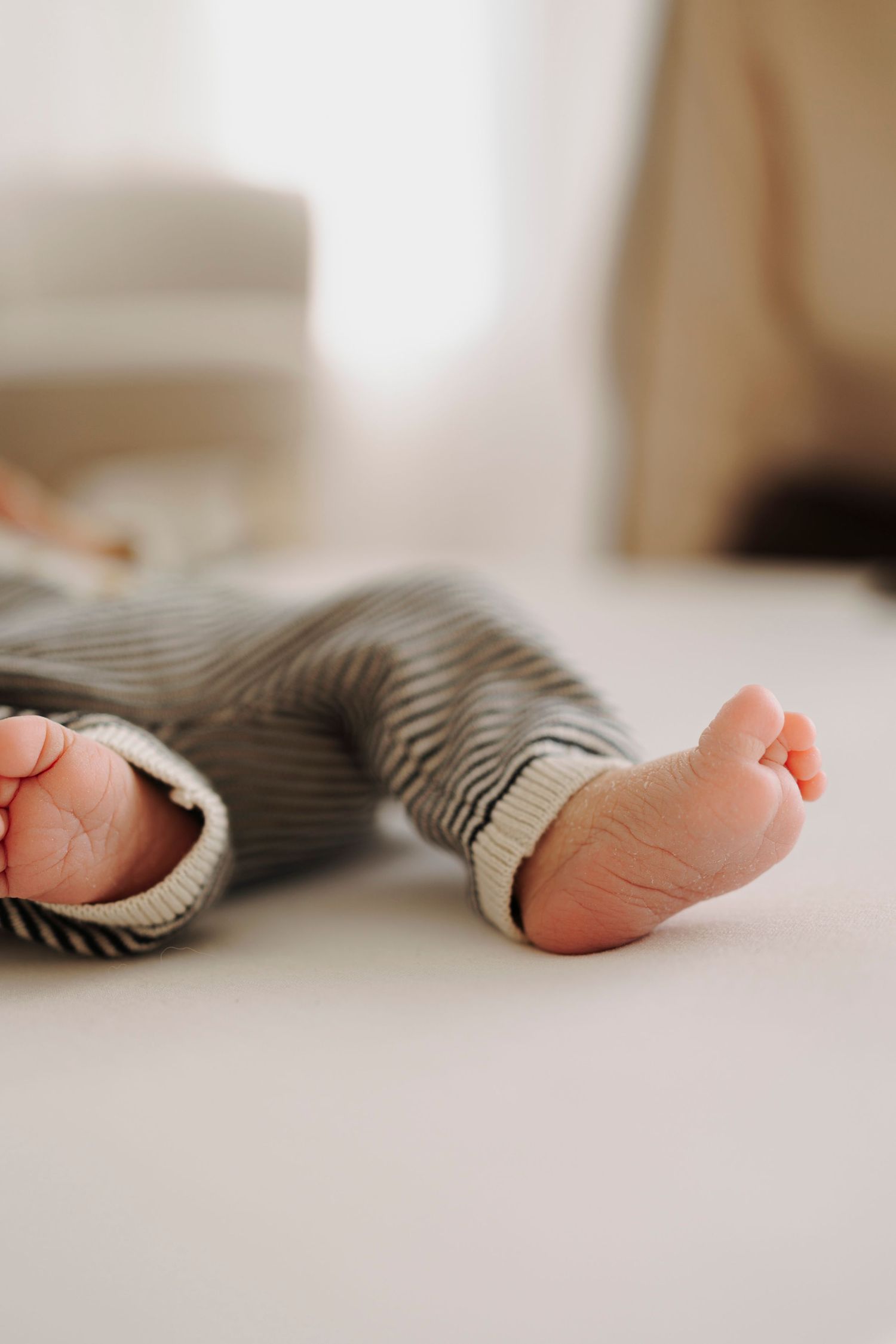 Tiny bare feet of a baby wearing striped pajamas lying on white bedding in soft natural light.