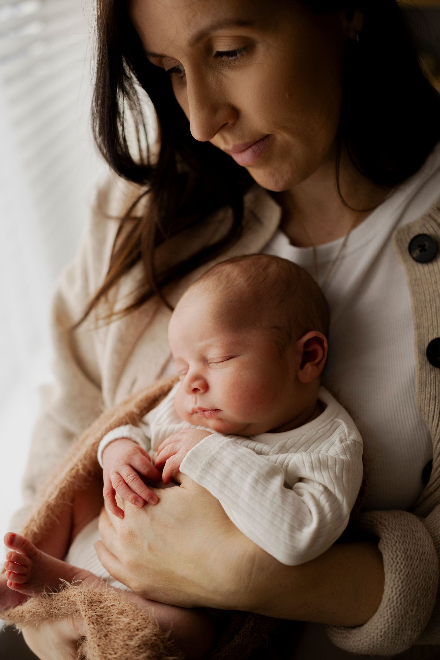 A tender moment between a mother and sleeping newborn baby in soft natural light.
