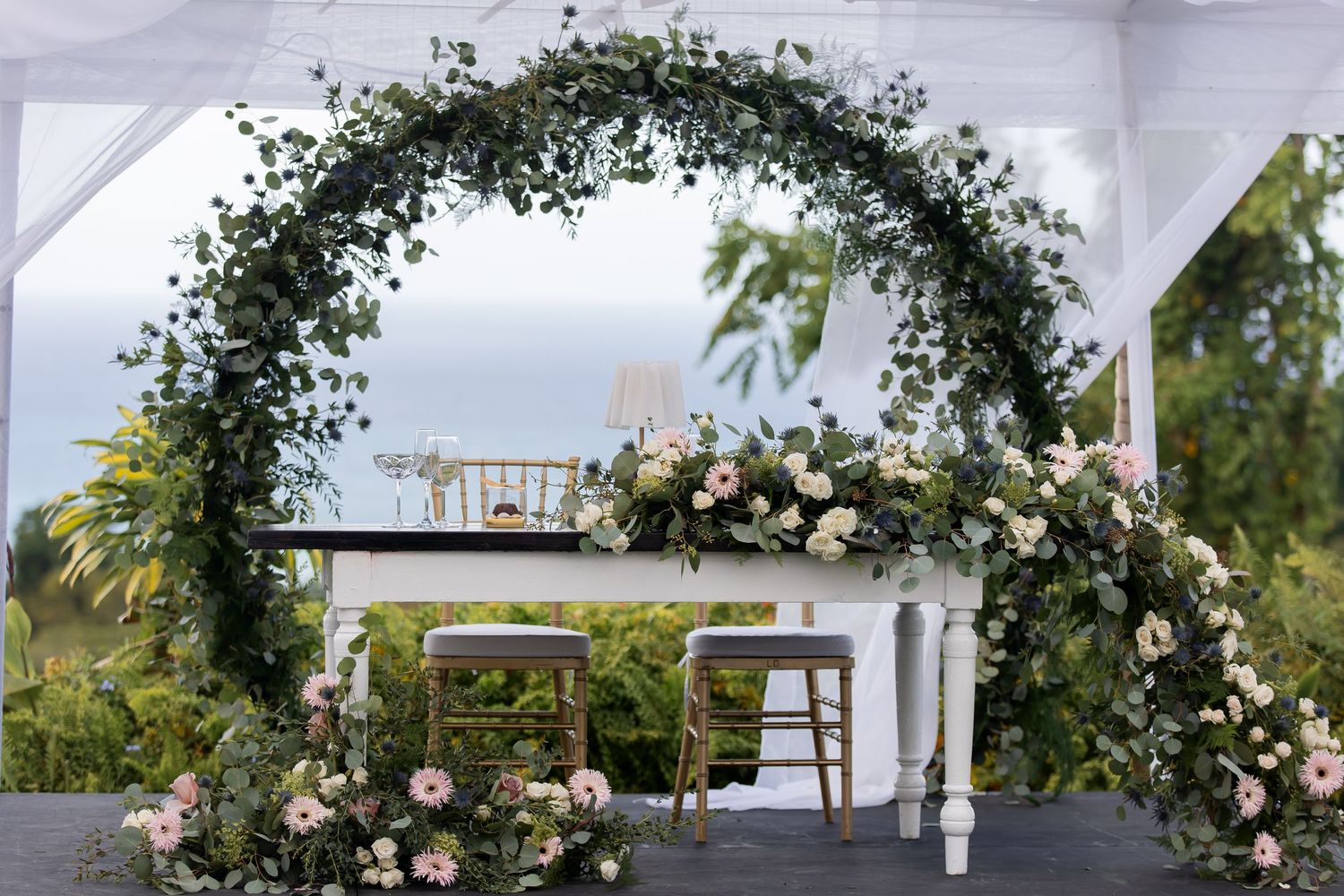 A lush floral arch with white and pink roses decorates an elegant outdoor wedding pergola structure.