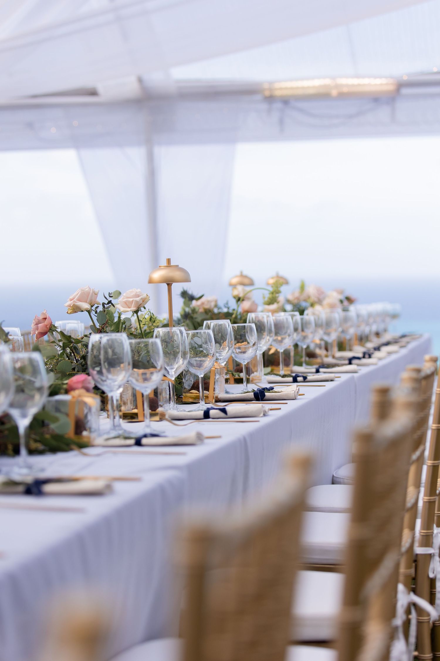 Elegant outdoor wedding table setting with wine glasses and floral centerpieces overlooking ocean view.