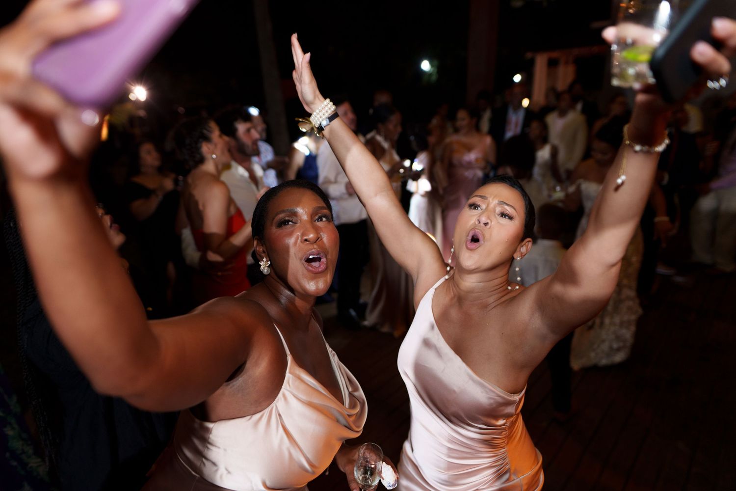 People dancing and celebrating at a lively nightclub or party with festive lighting and crowd in the background.