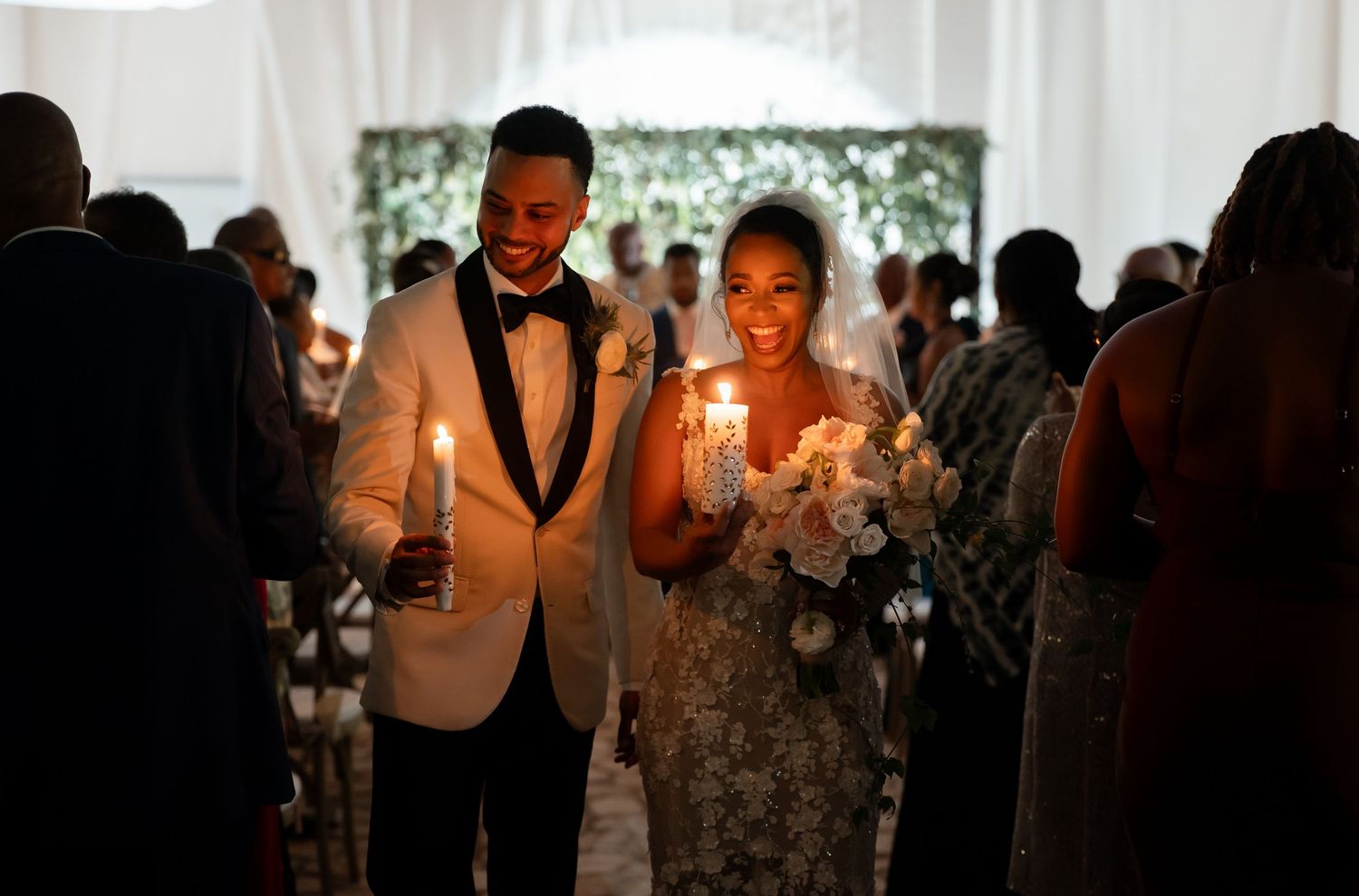 Wedding party attendees hold glowing sparklers during an evening wedding reception in an elegant white-draped venue.