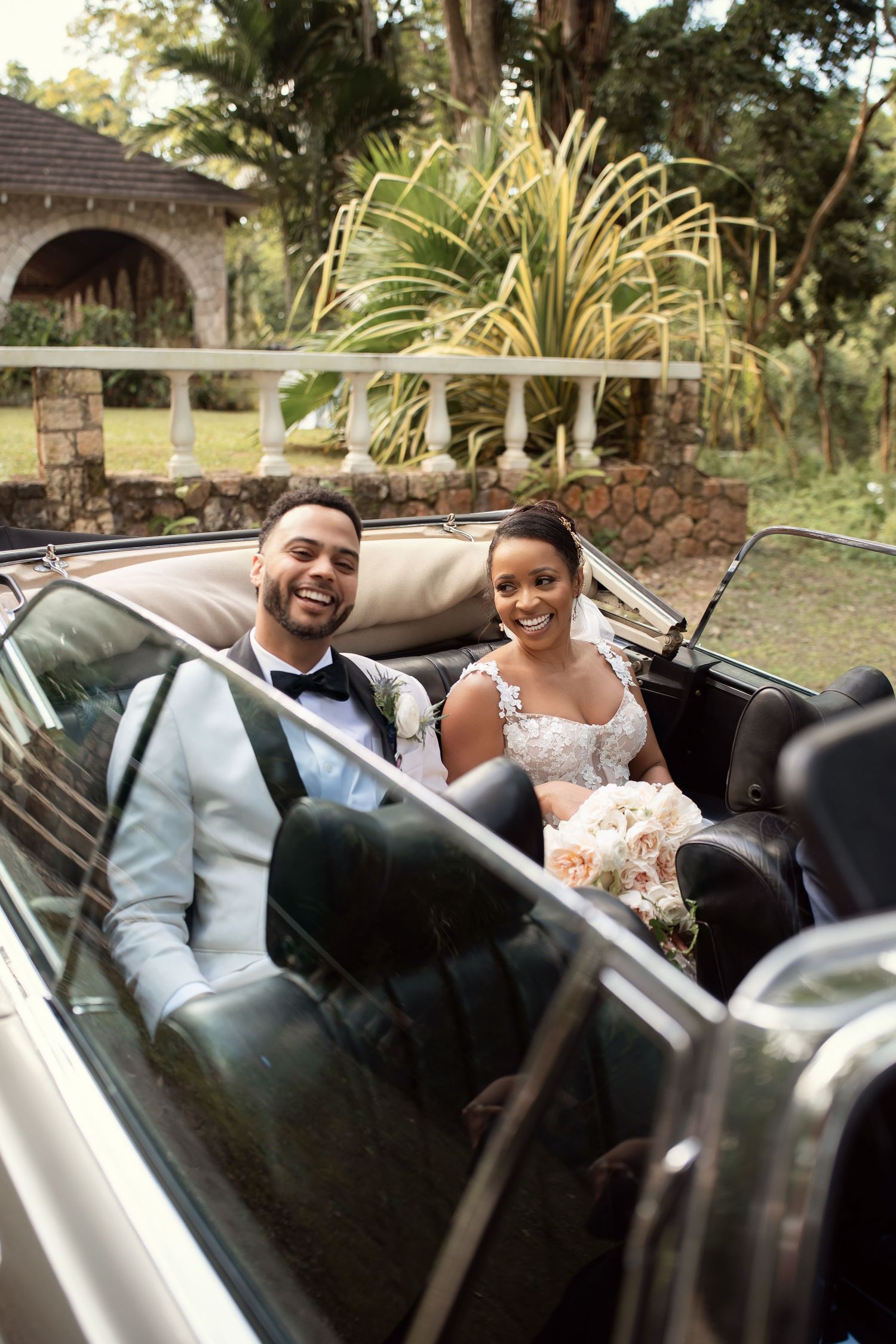 A happy couple sitting in a classic convertible car on their wedding day wearing formal attire.