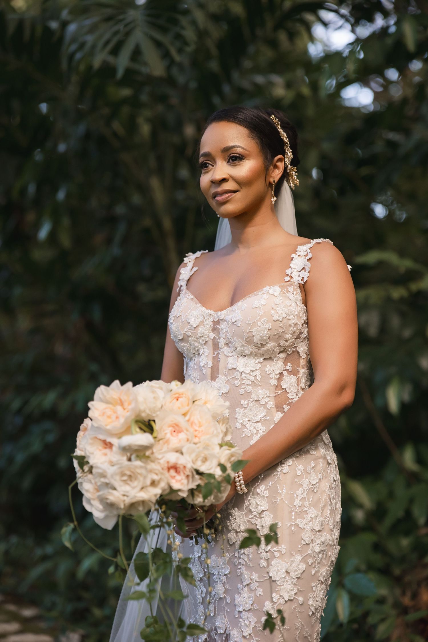 A beautiful wedding bouquet with white flowers is held against a lace wedding dress in a garden setting.