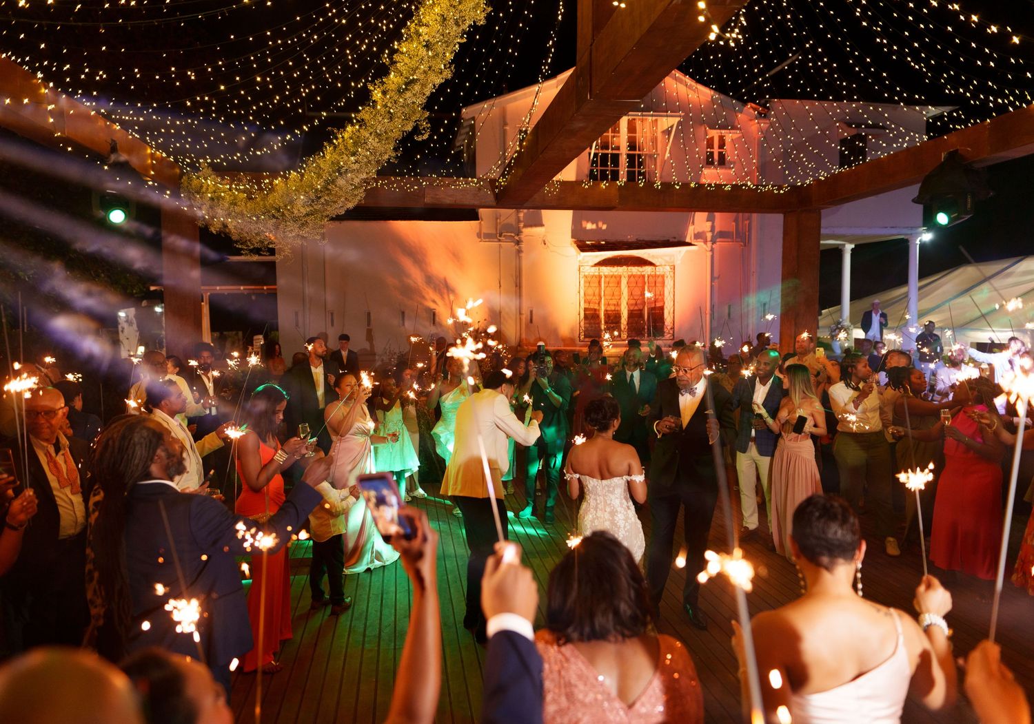 A lively evening wedding reception with string lights overhead and guests dancing under warm glowing decorations.