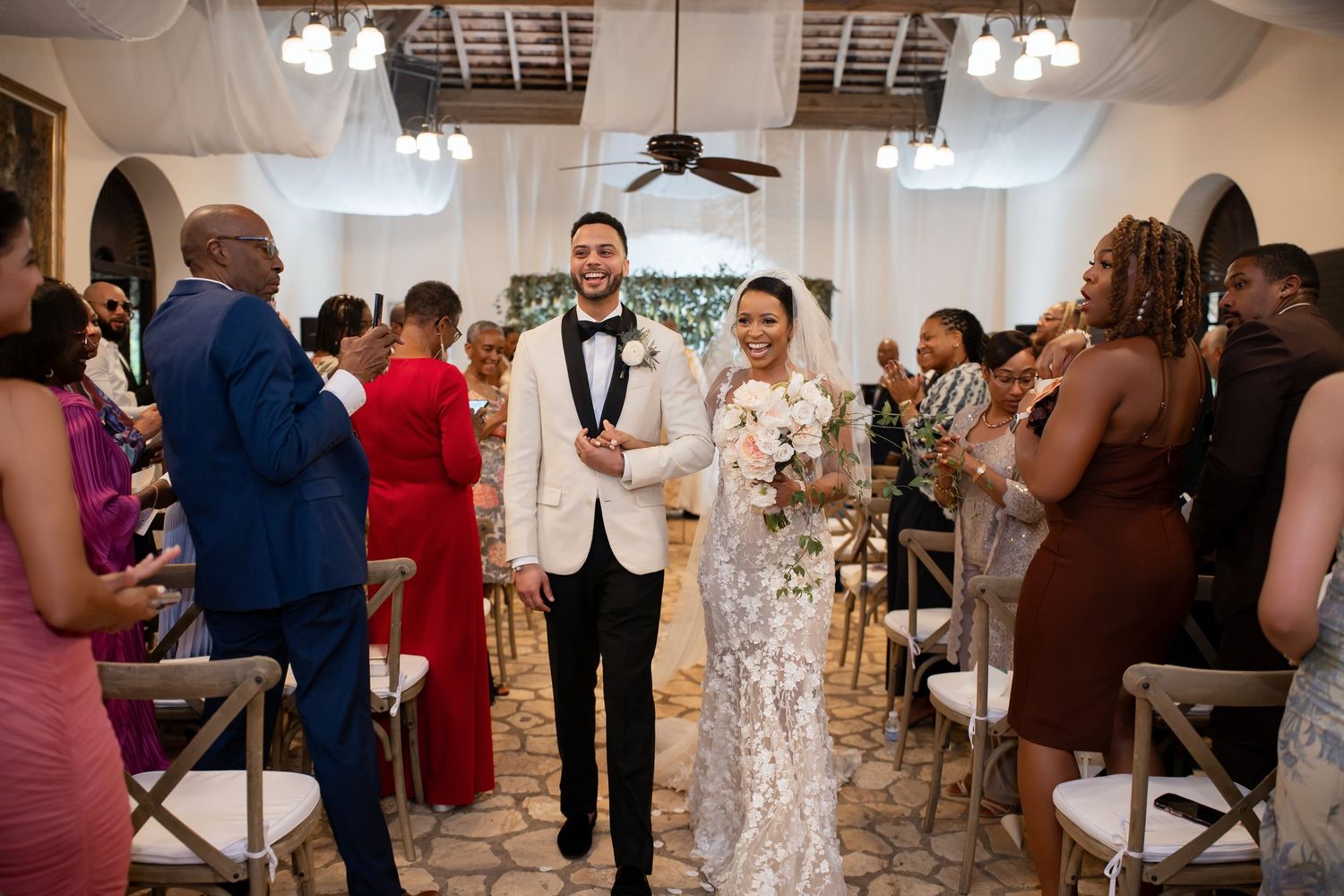 A joyful wedding couple walks down the aisle together while guests celebrate in an elegant indoor venue.