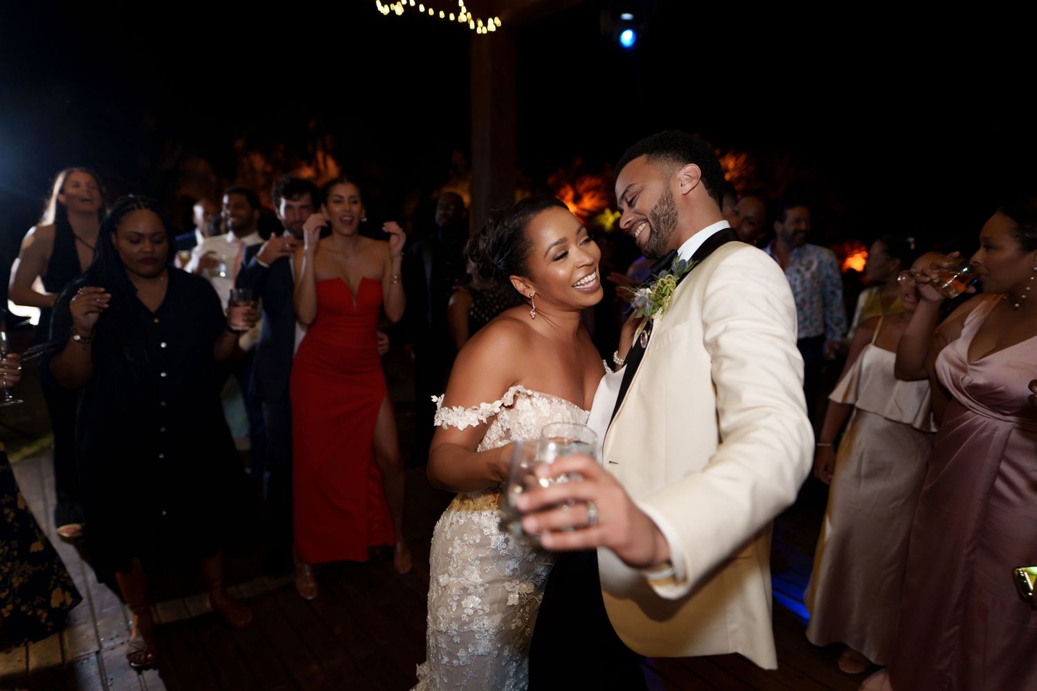 A couple shares their first dance at an evening wedding reception as guests look on with phones and cameras.