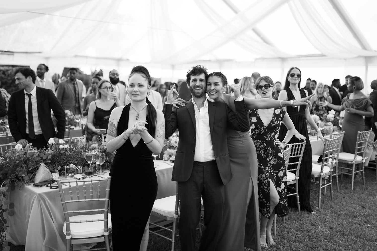 Wedding guests dance and celebrate together under a large white tent during an outdoor reception.