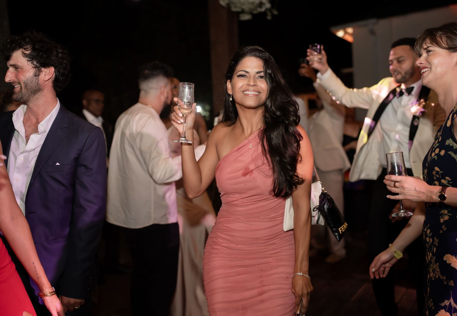 Wedding guests celebrate on the dance floor holding champagne glasses in a festive reception setting.