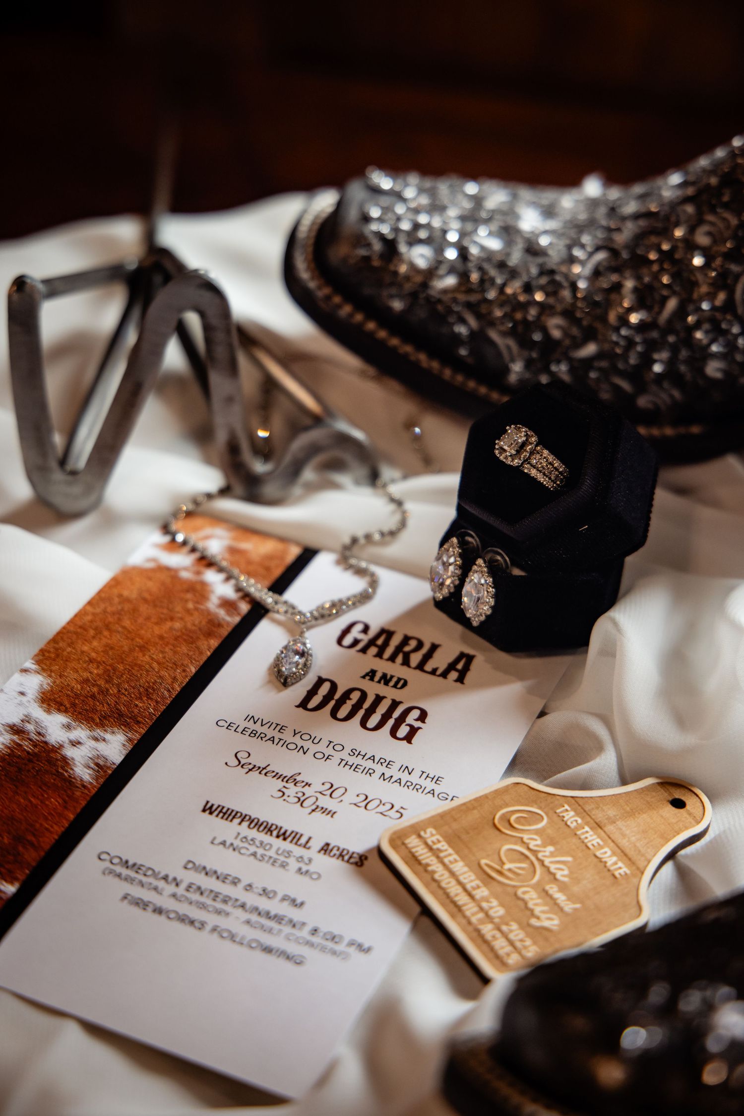 Western wedding flat lay featuring Carla and Doug invitation, diamond jewelry, cowboy boots, spurs, and wooden decor.