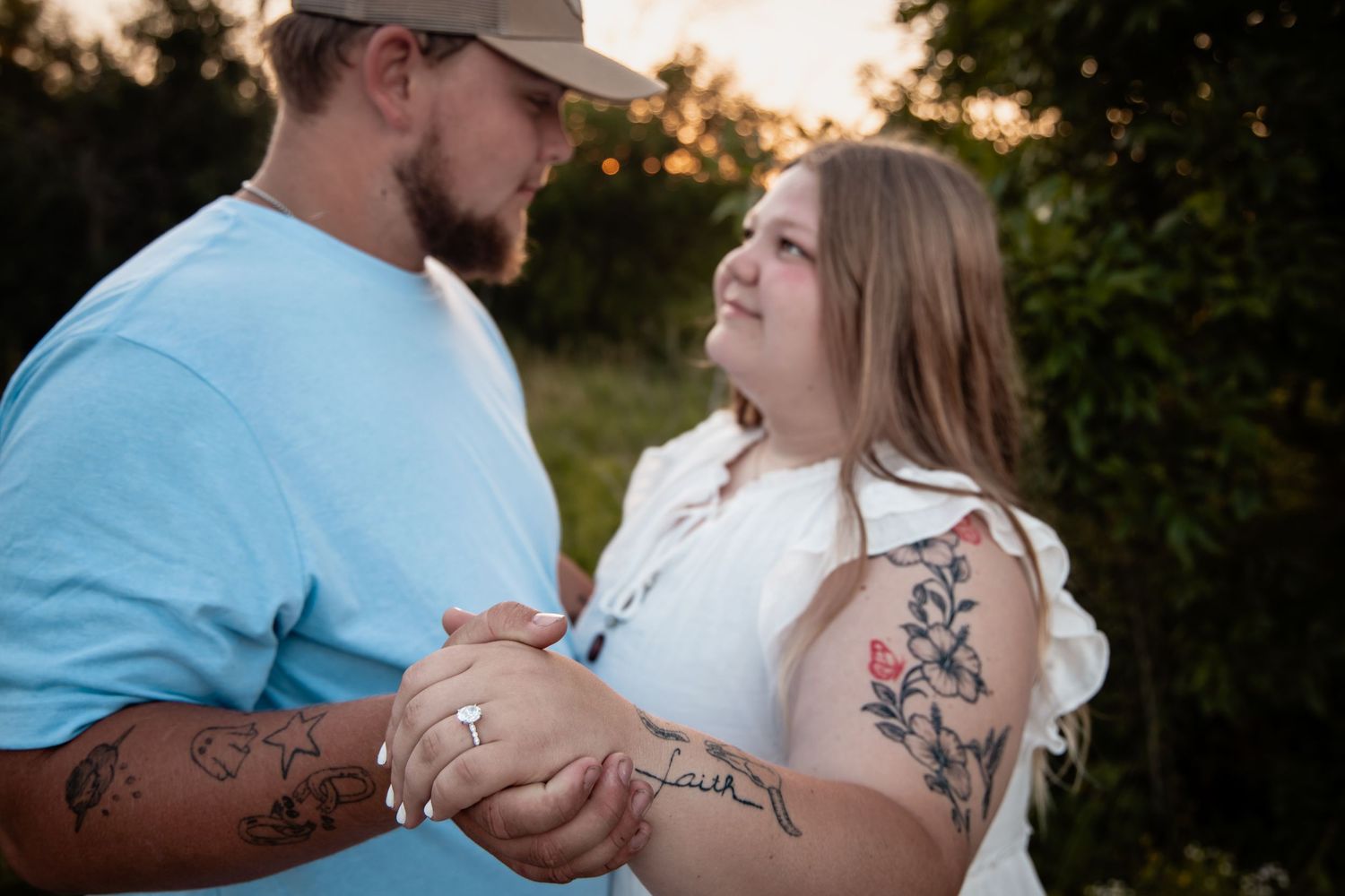 A couple with tattoos holds hands and gazes at each other lovingly outdoors at golden hour.