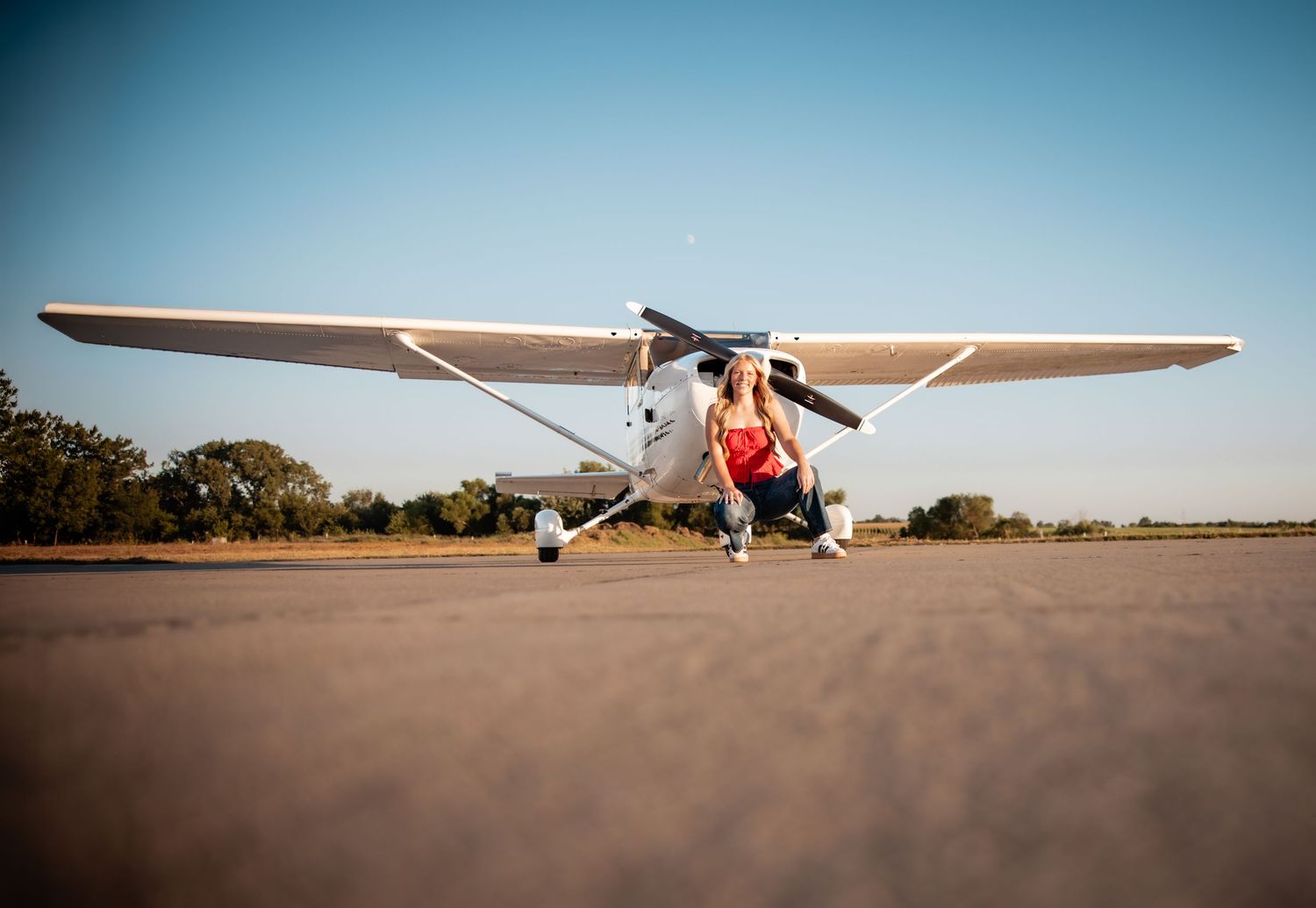 Woman posing in front of a small Cessna aircraft on a sunny airstrip with clear blue skies.