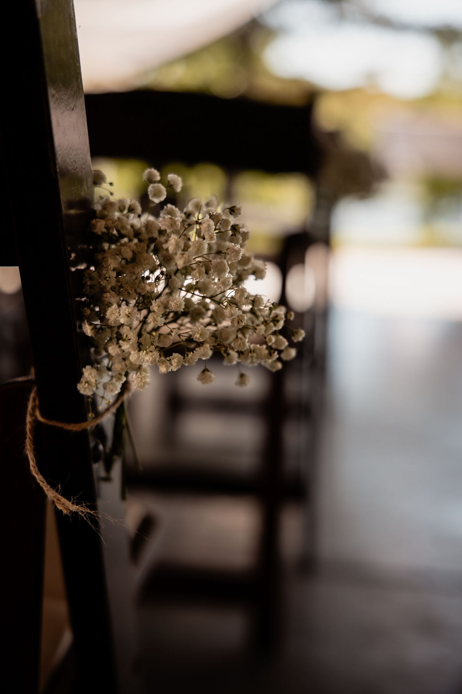 Dried baby's breath bouquet tied with twine on dark wooden wedding ceremony chair aisle decoration.
