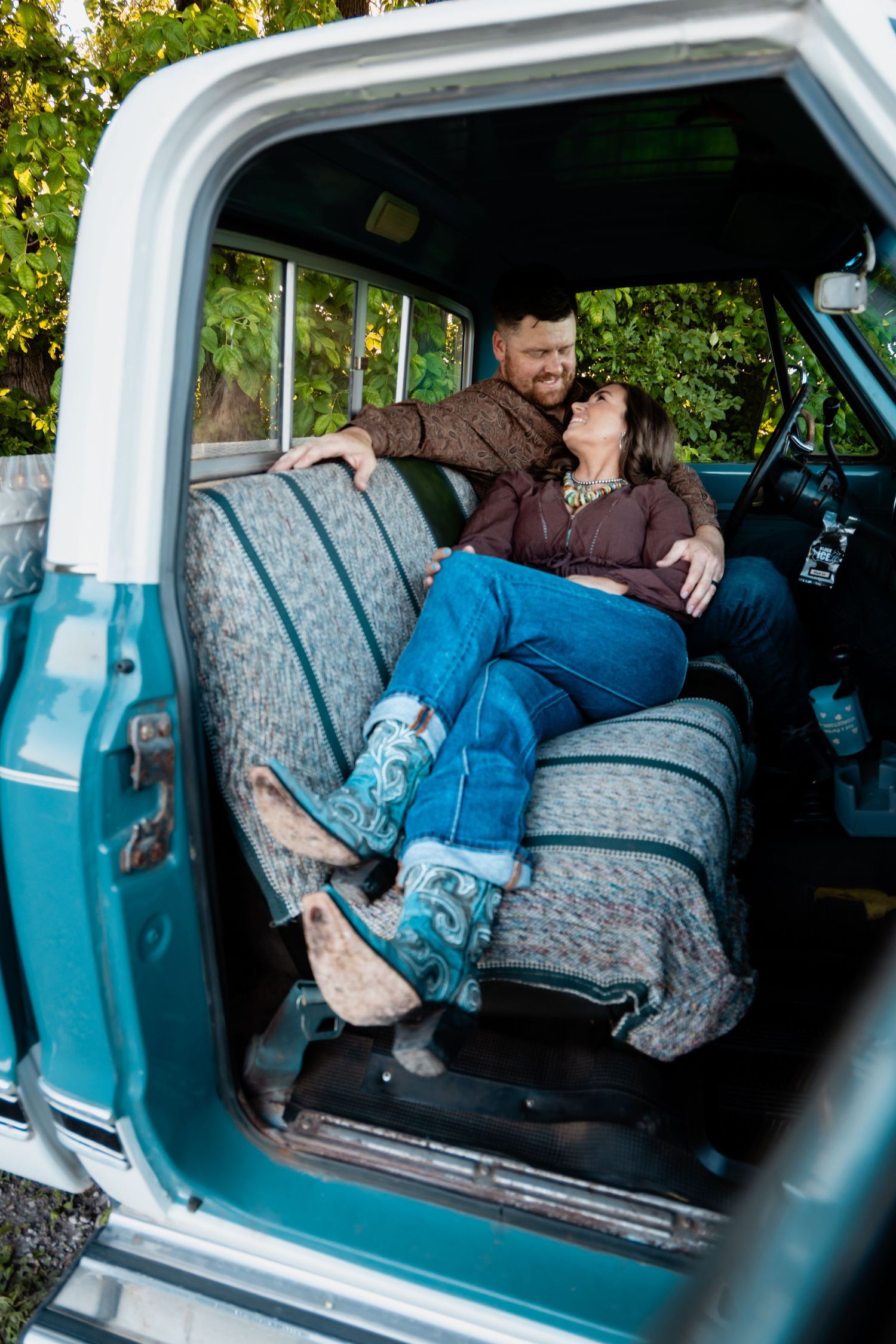 Couple laughing together on the bench seat of a vintage teal pickup truck.