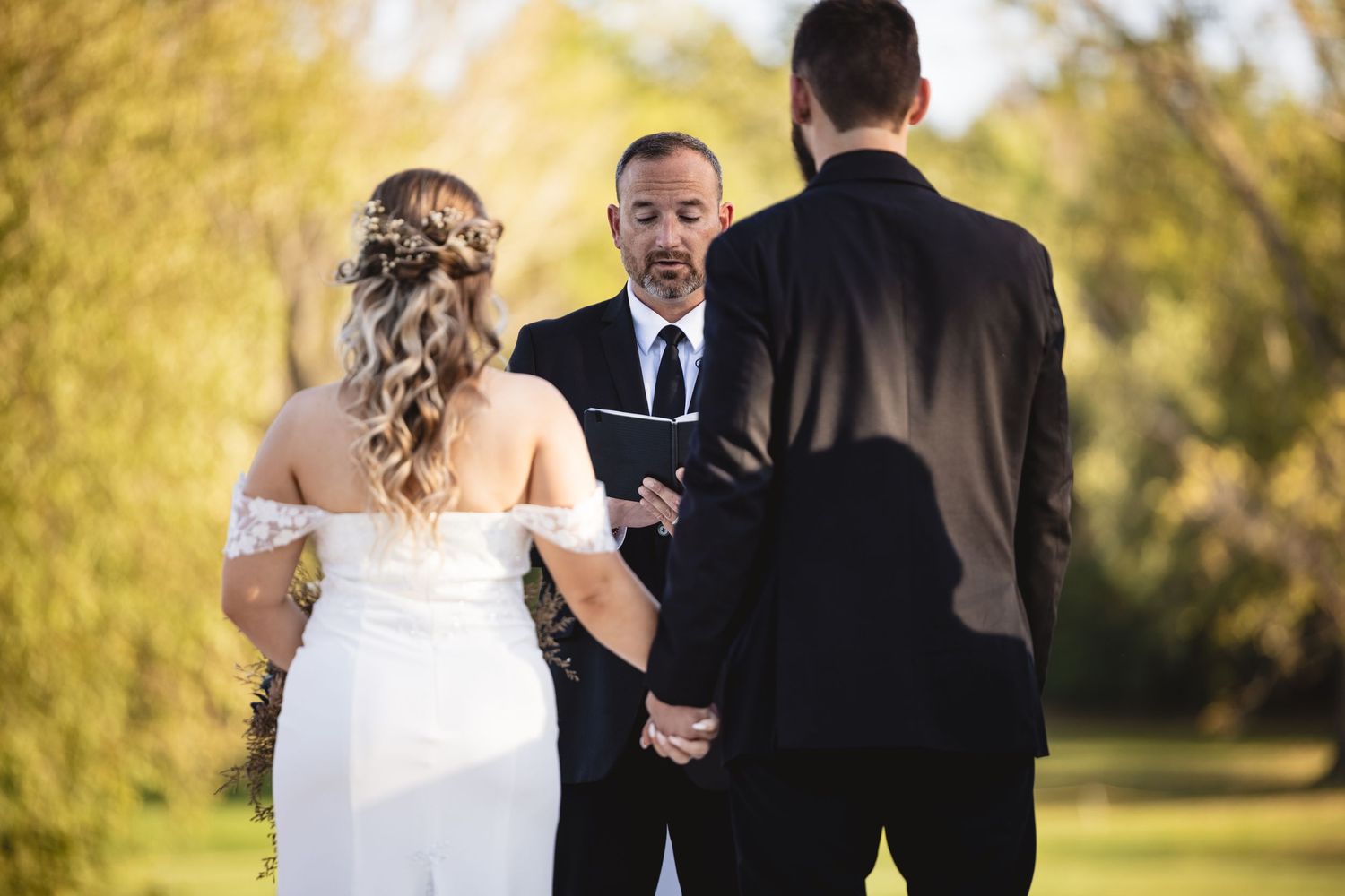 Bride and groom exchange vows with officiant during an outdoor wedding ceremony.