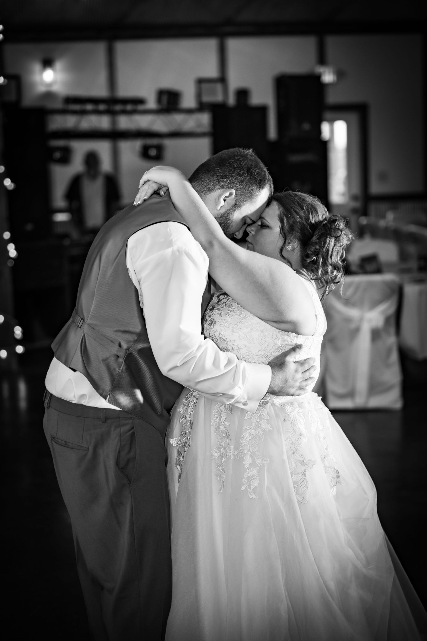 Black and white photo of bride and groom sharing their first dance, embracing closely at wedding reception.