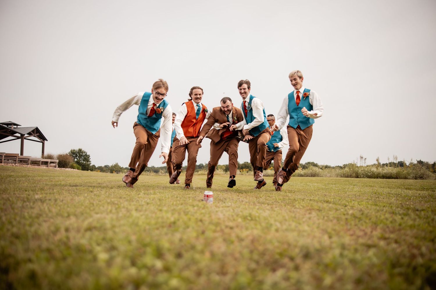 Five children in matching vests and ties run joyfully across a green field at an outdoor event.